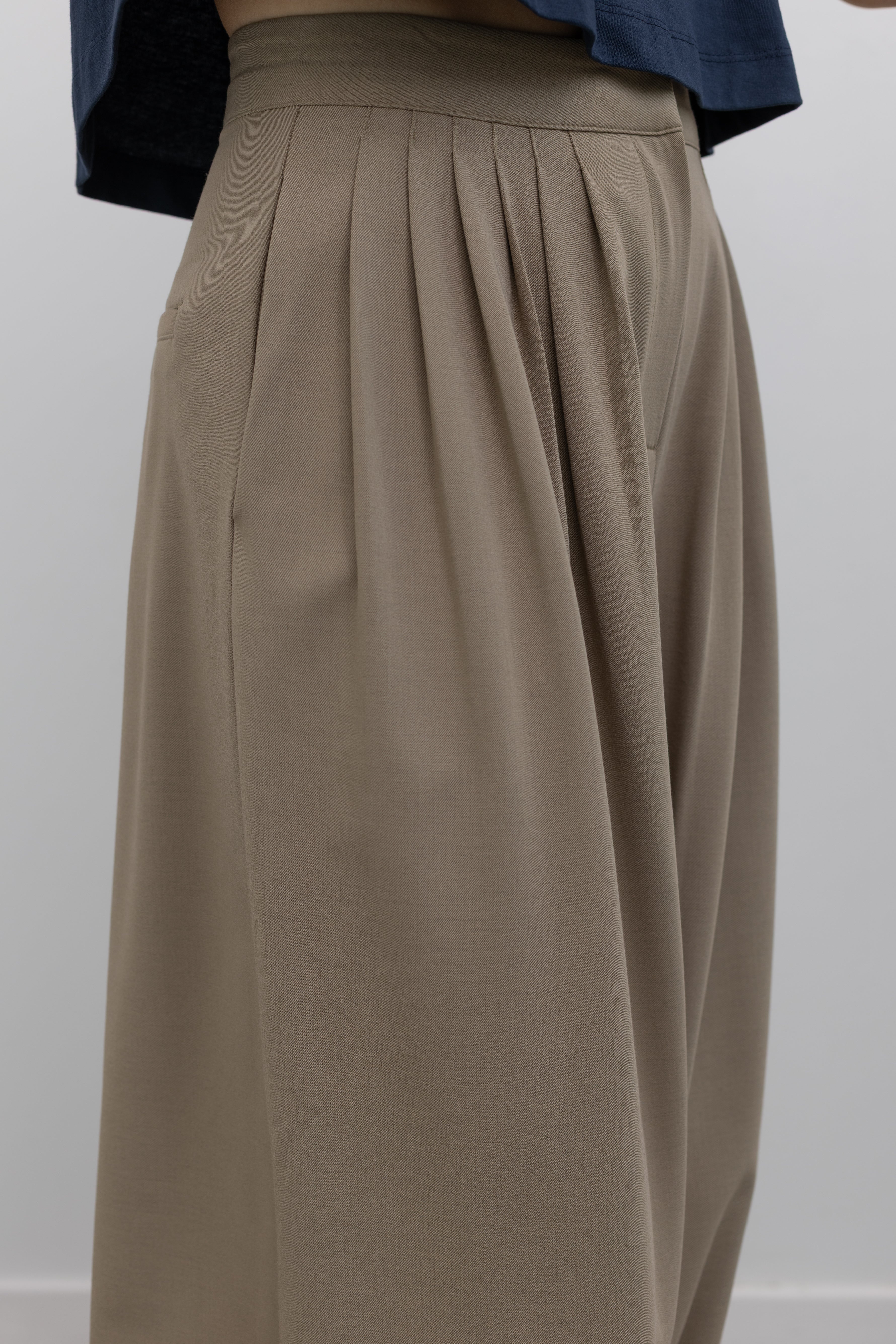 Close-up view of pleat and pocket details on the refined and sophisticated Collective brand beige Tores pleat front harem pant featuring a cinched elastic ankle creating a balloon silhouette at an Alas Eius store.