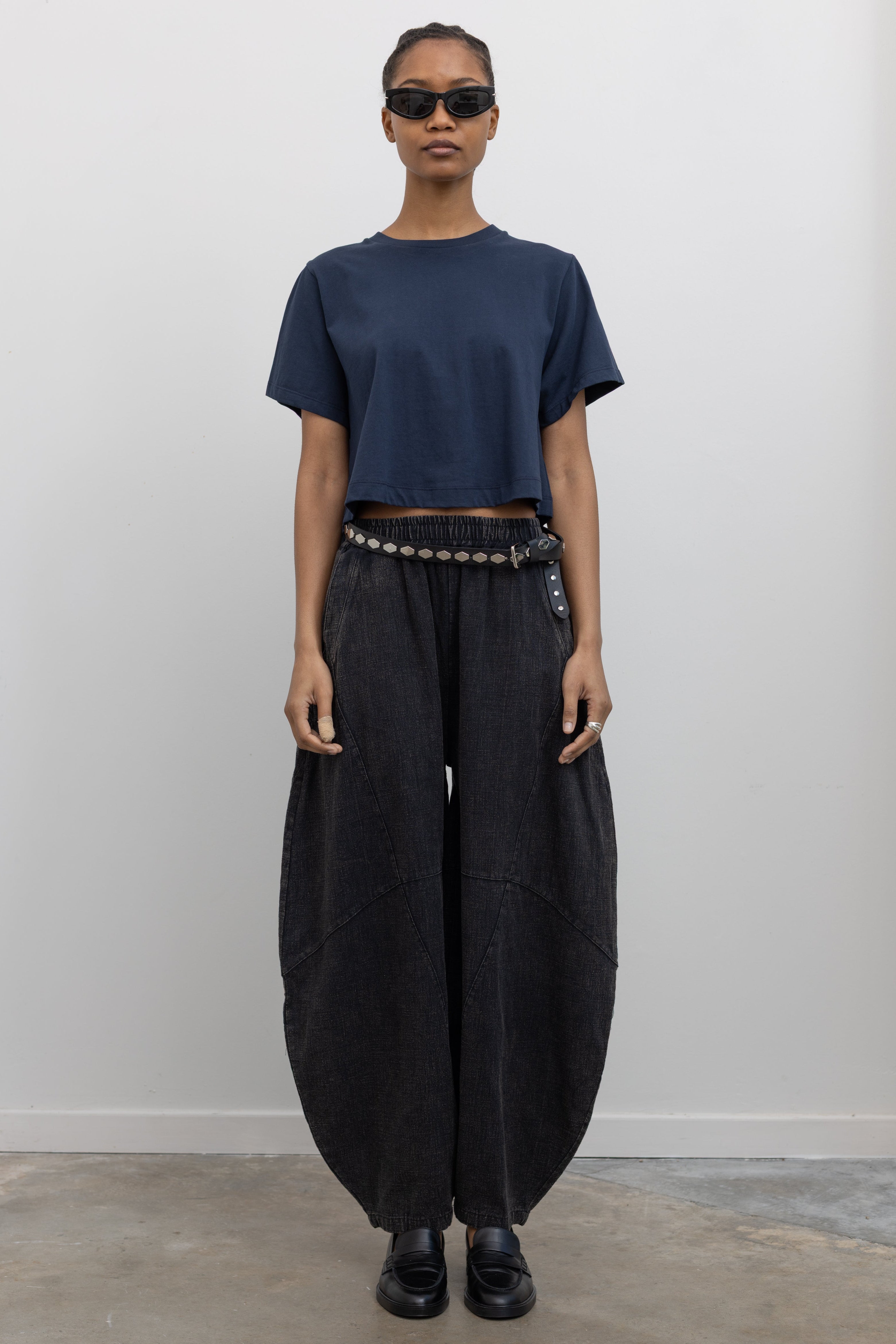 Full length front view of a woman wearing spring contemporary fashion in a Alas Eius label navy blue cropped t-shirt paired with Collective Spring Black Barrel Cotton Blend Pants at Alas Eius. 