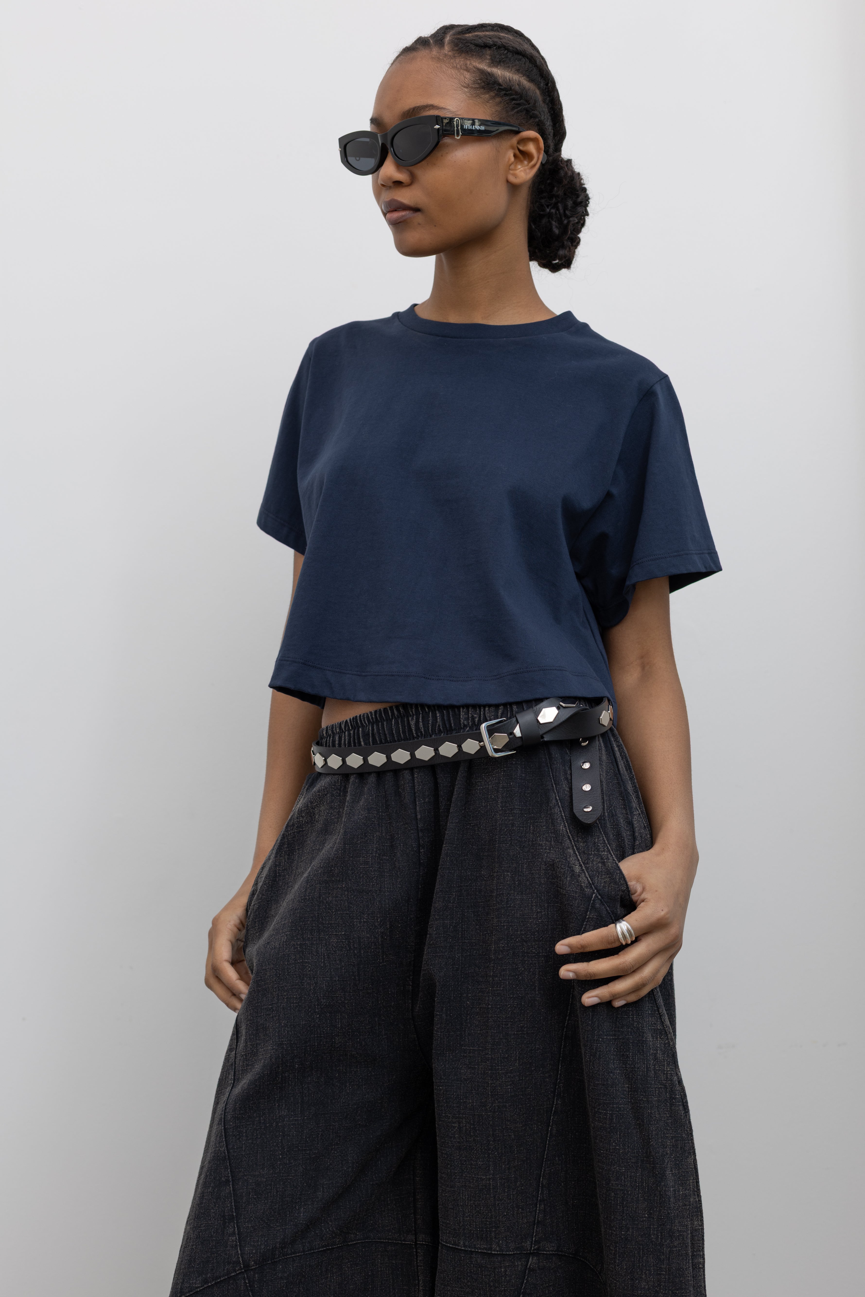 Close-up 3/4 of a woman wearing spring contemporary fashion in a Alas Eius label navy blue cropped t-shirt paired with Collective Spring Black Barrel Cotton Blend Pants at Alas Eius. 
