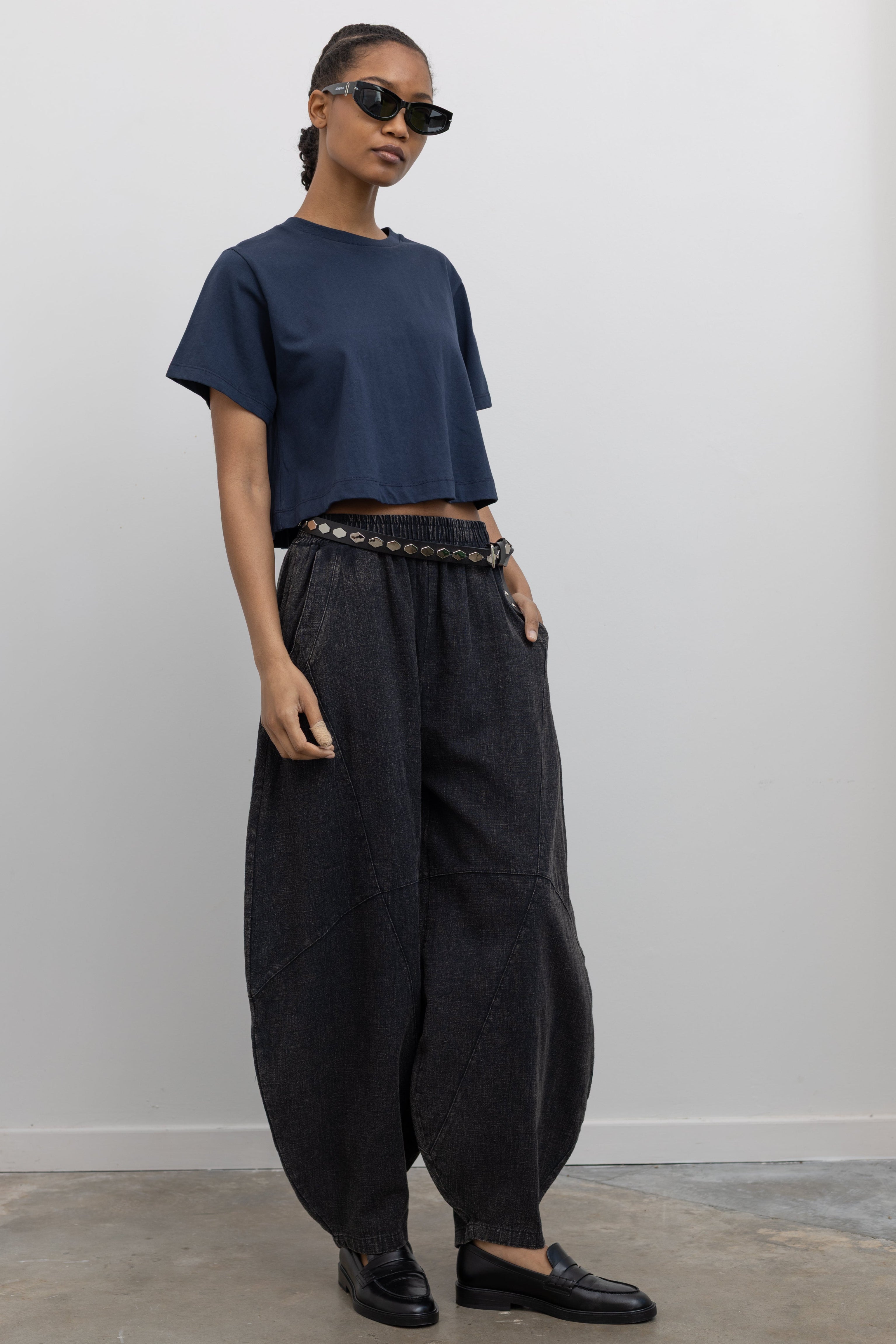 Full length 3/4 view of a woman wearing spring contemporary fashion in a Alas Eius label navy blue cropped t-shirt paired with Collective Spring Black Barrel Cotton Blend Pants at Alas Eius. 