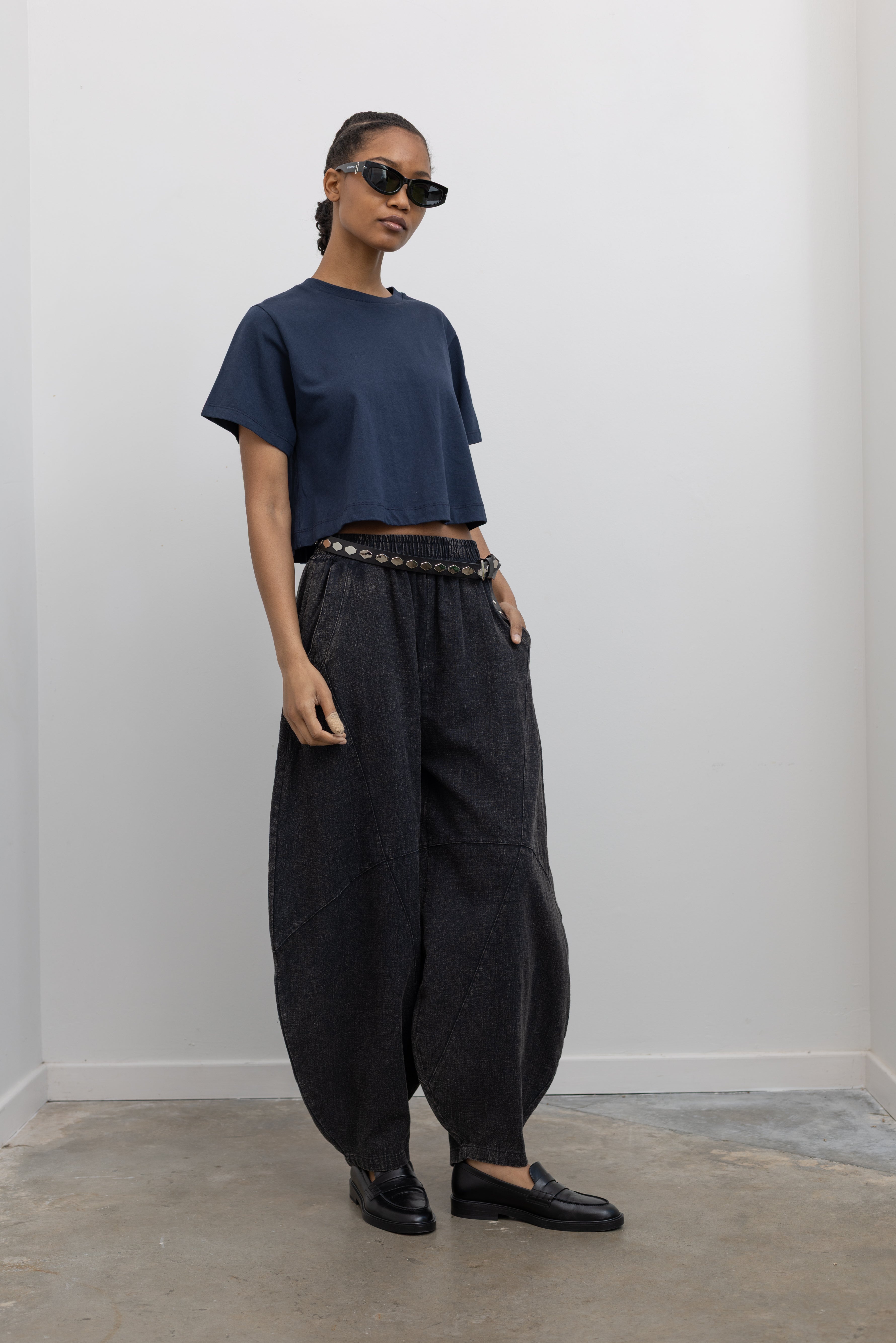 Full length 3/4 view of a woman wearing spring contemporary fashion in a Alas Eius label navy blue cropped t-shirt paired with Collective Spring Black Barrel Cotton Blend Pants at Alas Eius. 