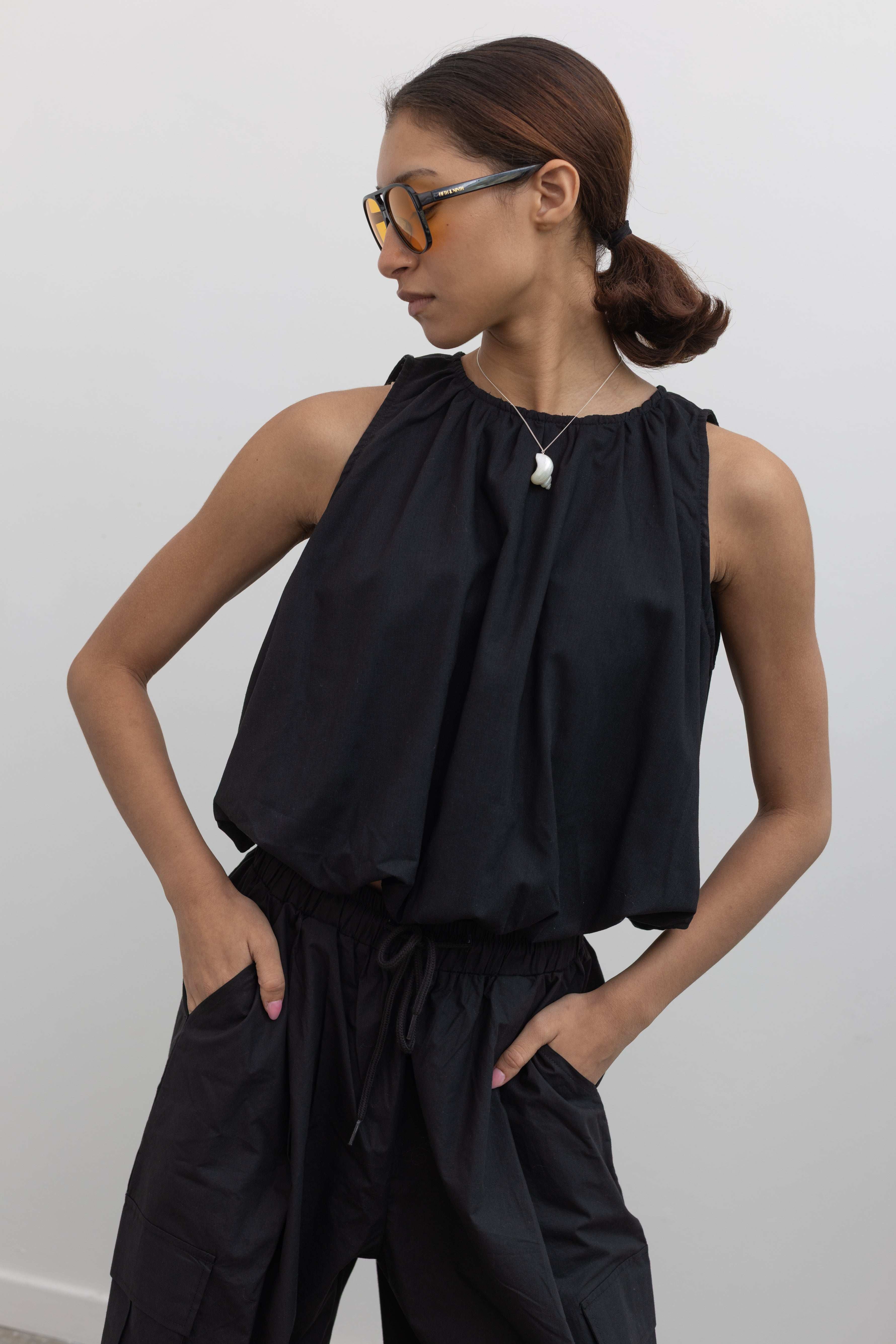 Woman posing wearing Spring fashion in a Collective black linen bubble hem sleeveless top paired with Alas Eius label black cargo pants 