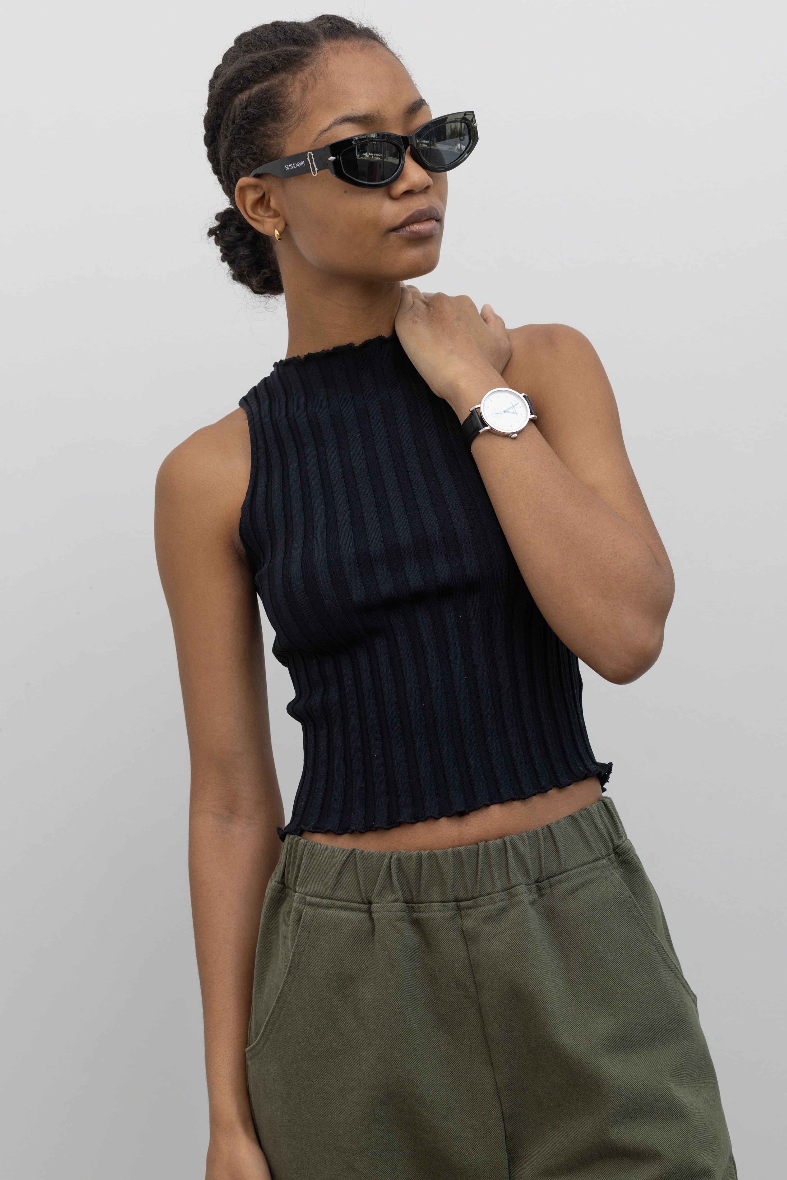 Close-up front view of a woman wearing spring capsule wardrobe essential in a Collective brand black fitted ribbed knit lettuce hem sleeveless top with slight mock neck paired with Le Bon Shoppe olive green cotton canvas arc shaped pant at Alas Eius. 