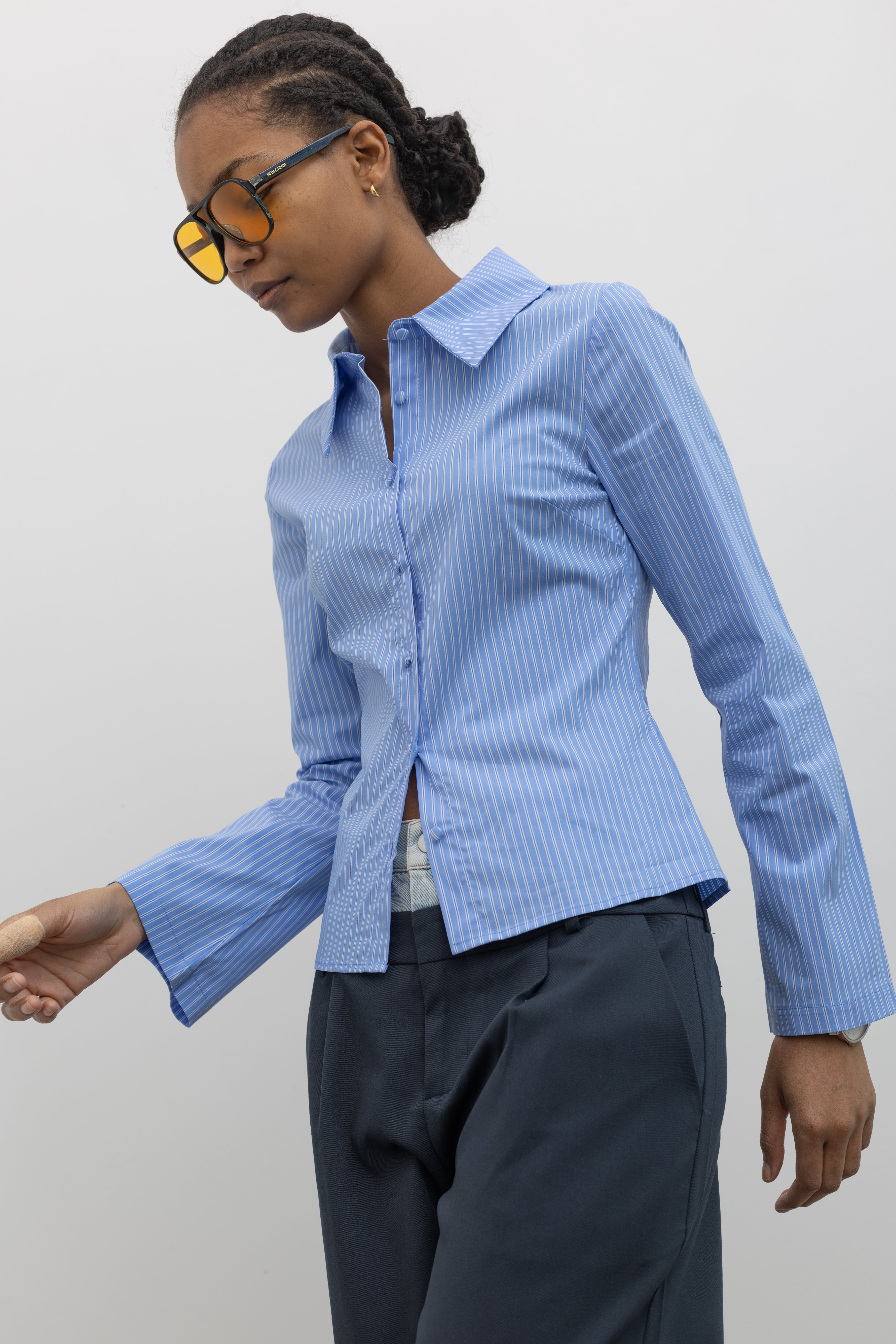 Side view of a woman in motion wearing Spring fashion in a Collective Blue Pinstripe Tailored Slim-Fit Button Down Top with flared sleeves and fabric covered buttons at Alas Eius.