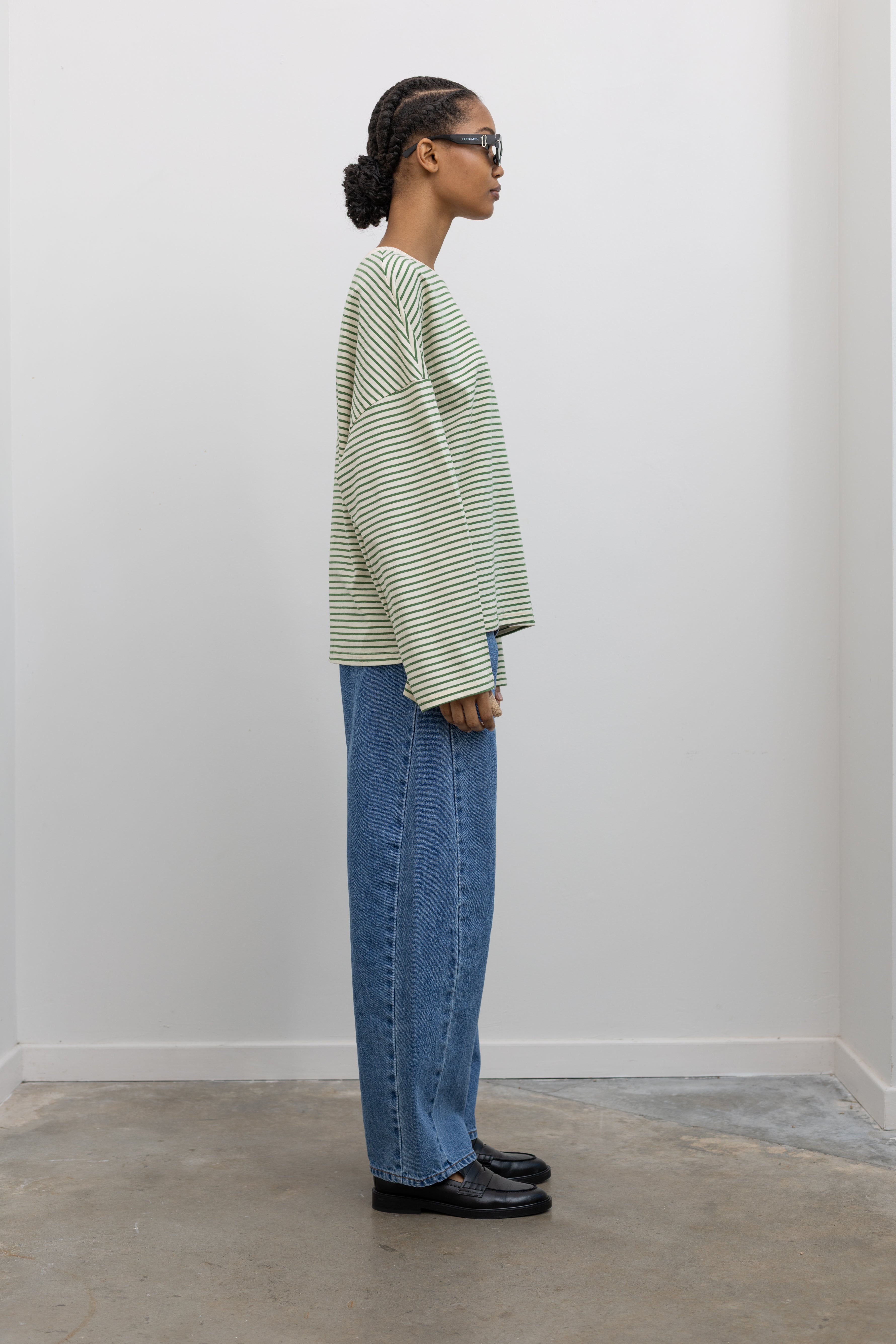 Full side view of a woman standing wearing Spring casual fashion in a Collective green and natural stripe dropped shoulder long sleeve cotton  oversized top paired with light wash denim at Alas Eius.