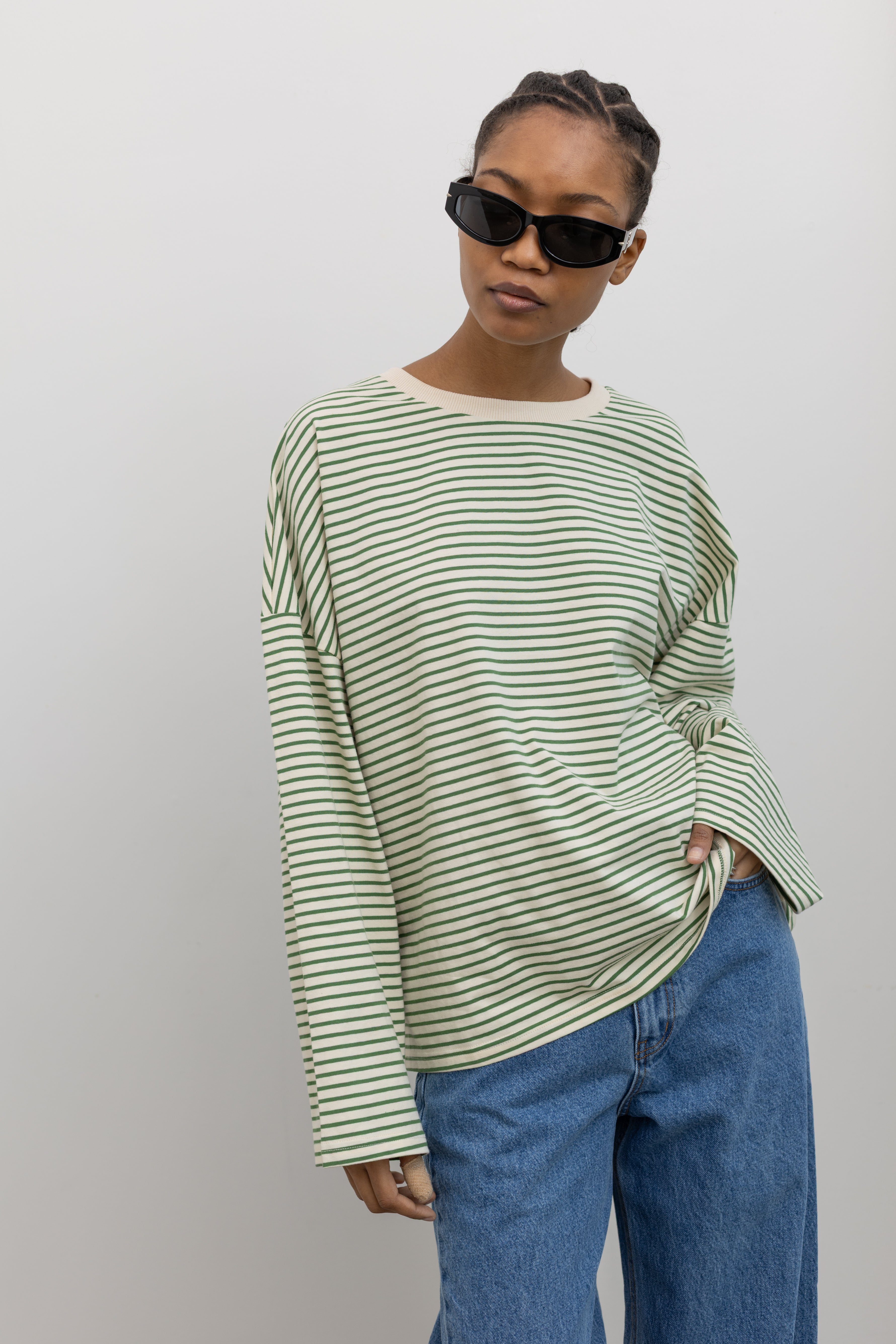 Front view of a woman standing wearing Spring casual fashion in a Collective green and natural stripe dropped shoulder long sleeve cotton  oversized top paired with light wash denim at Alas Eius.