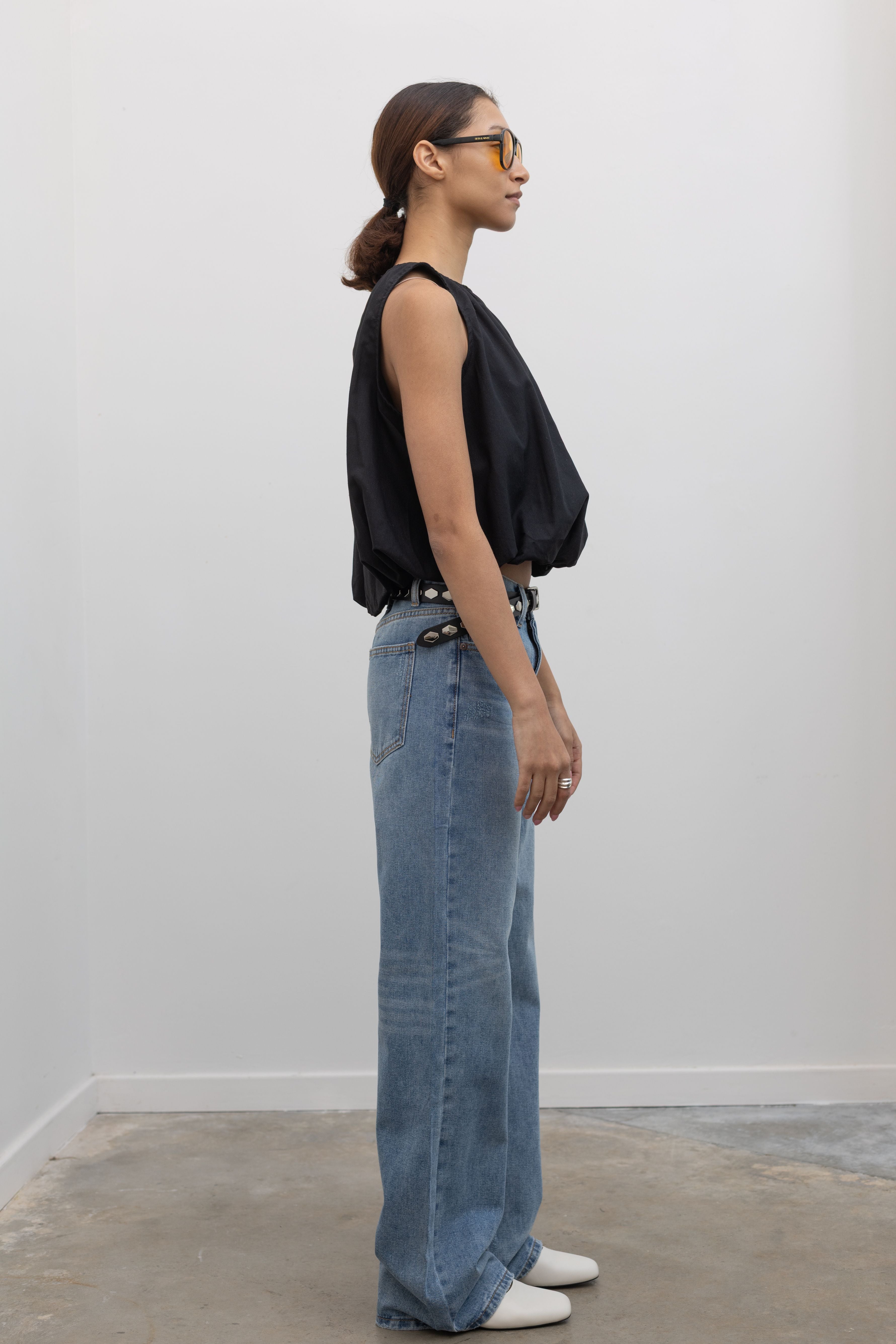 Side view of Woman standing wearing Spring fashion in a black gathered neck and balloon hem top with a pair of Collective Light Wash Slouchy Mid Rise Jeans at Alas Eius 