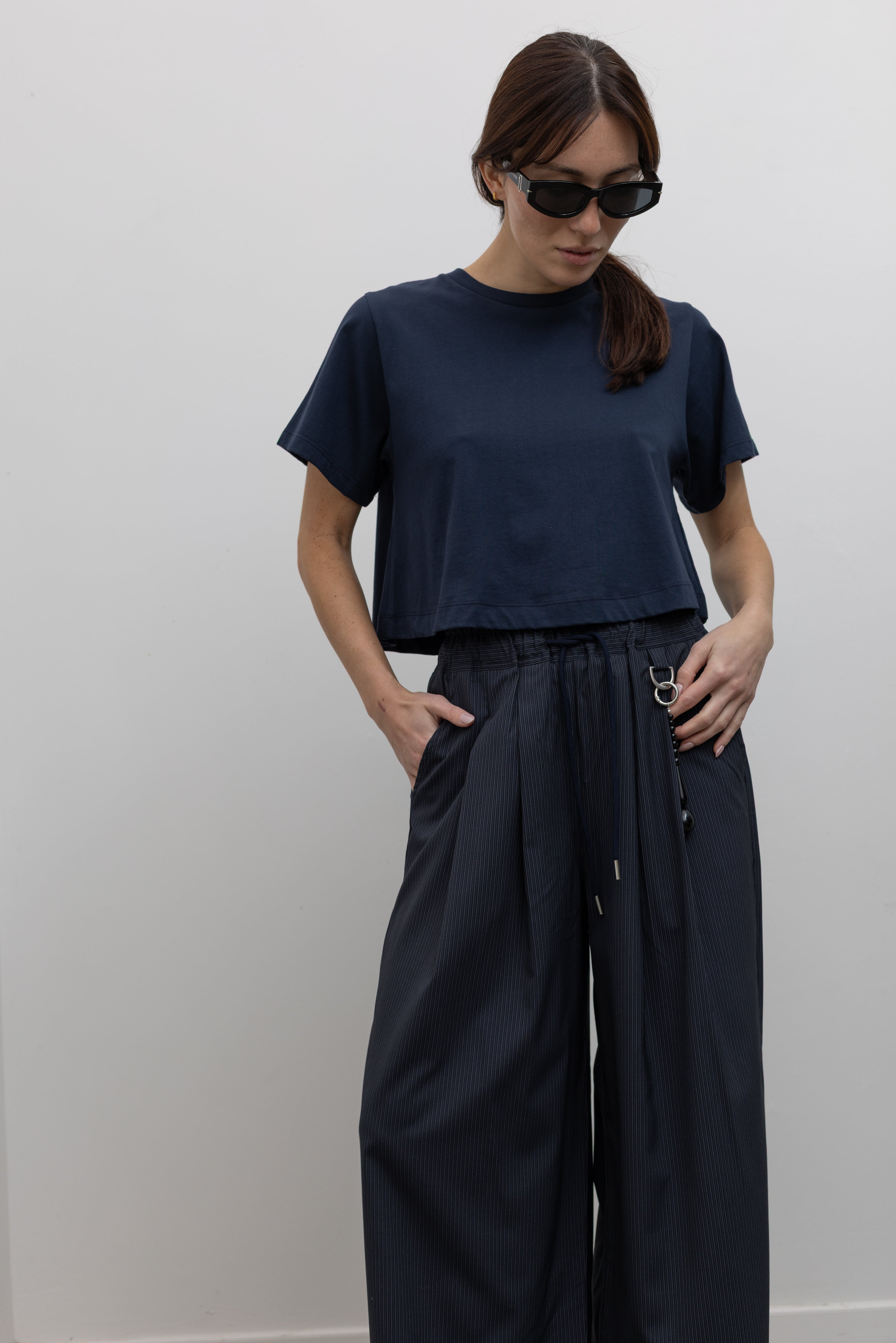 Woman standing wearing Spring fashion in a pair of Collective Navy Pinstripe Wide Leg Drawstring Pants and navy blue tee with black leather sandals at Alas Eius