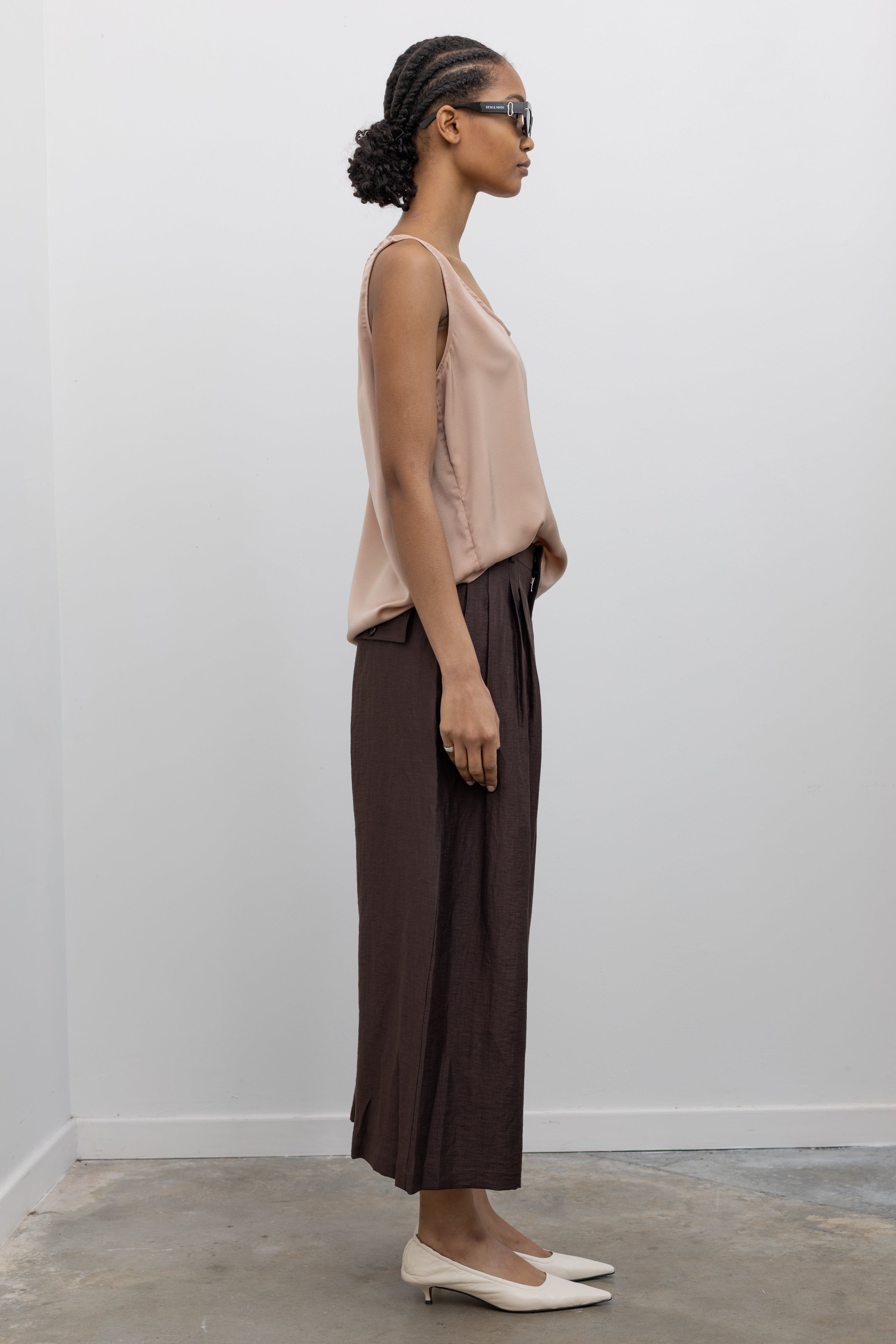 Side view of a woman wearing Spring fashion in a Collective brand solid beige satin tank top with a relaxed flowy fit paired with pleated trouser at Alas Eius.