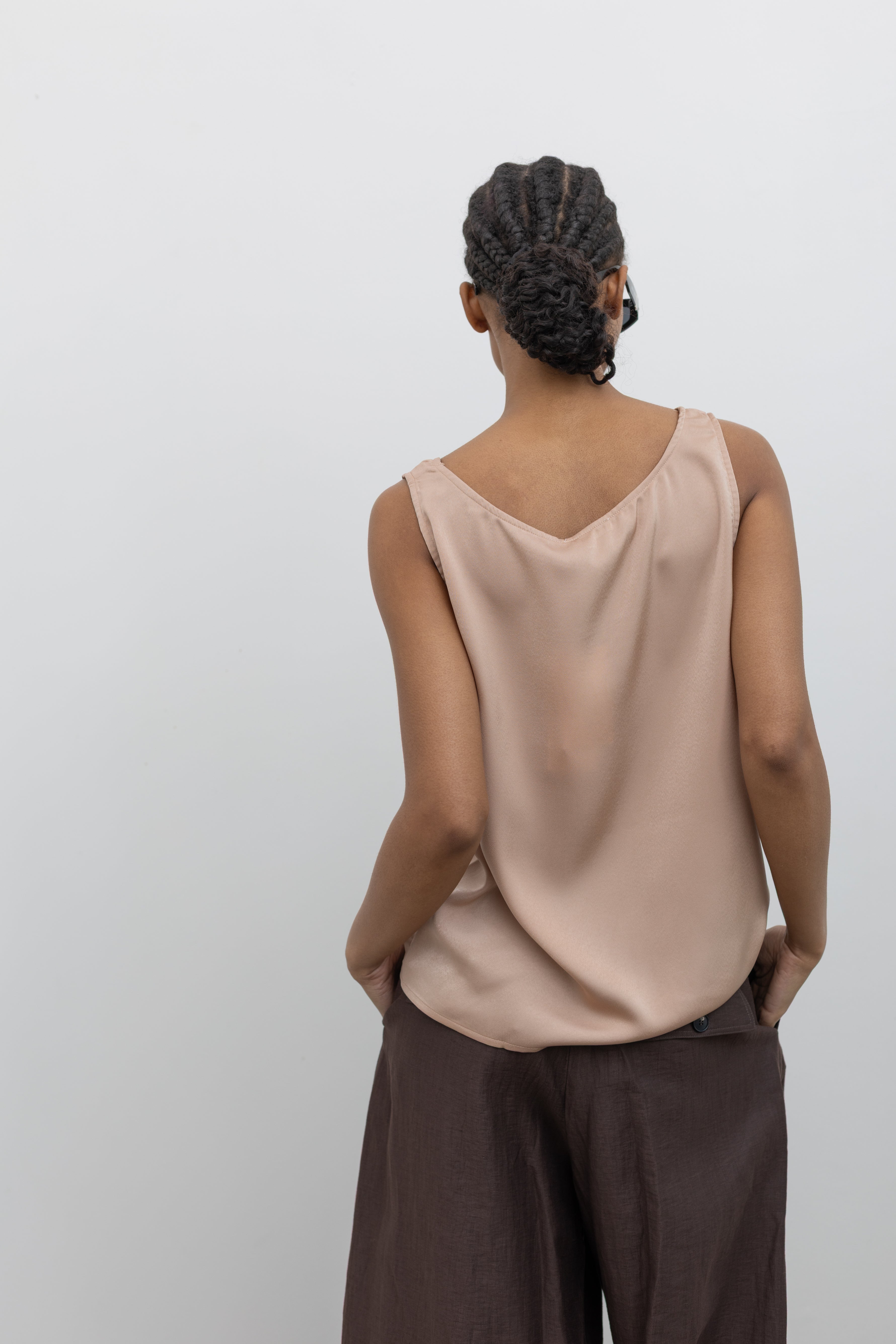 Close-up back view of a woman wearing Spring fashion in a Collective brand solid beige satin tank top with a relaxed flowy fit paired with pleated trousers at Alas Eius.