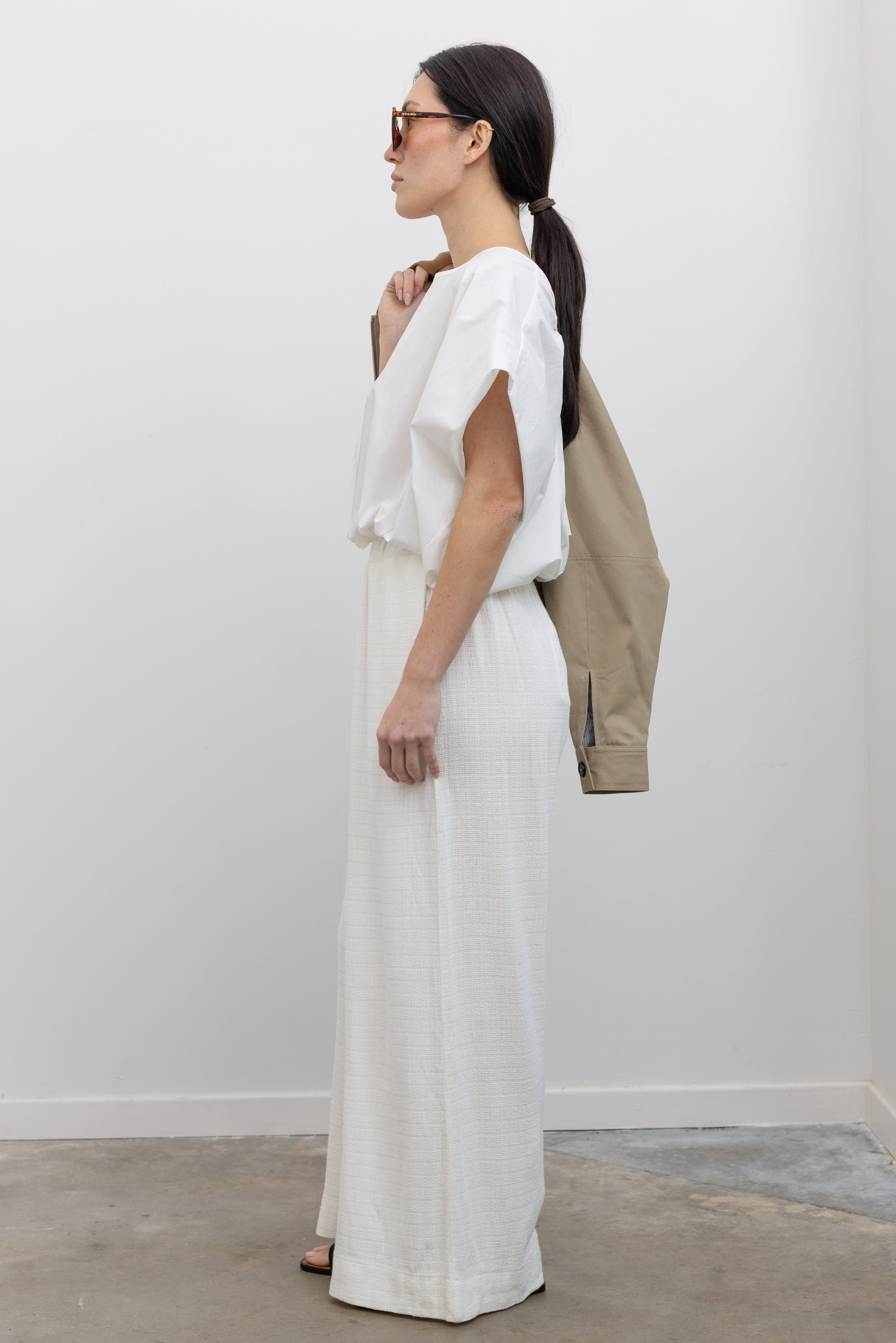 Full length side view of woman in motion wearing chic spring fashion in Collective Ivory Linen Wide Leg Pants featuring an elastic waistband and side seam pockets paired with an oversized short sleeve top and strappy leather sandals at Alas Eius.