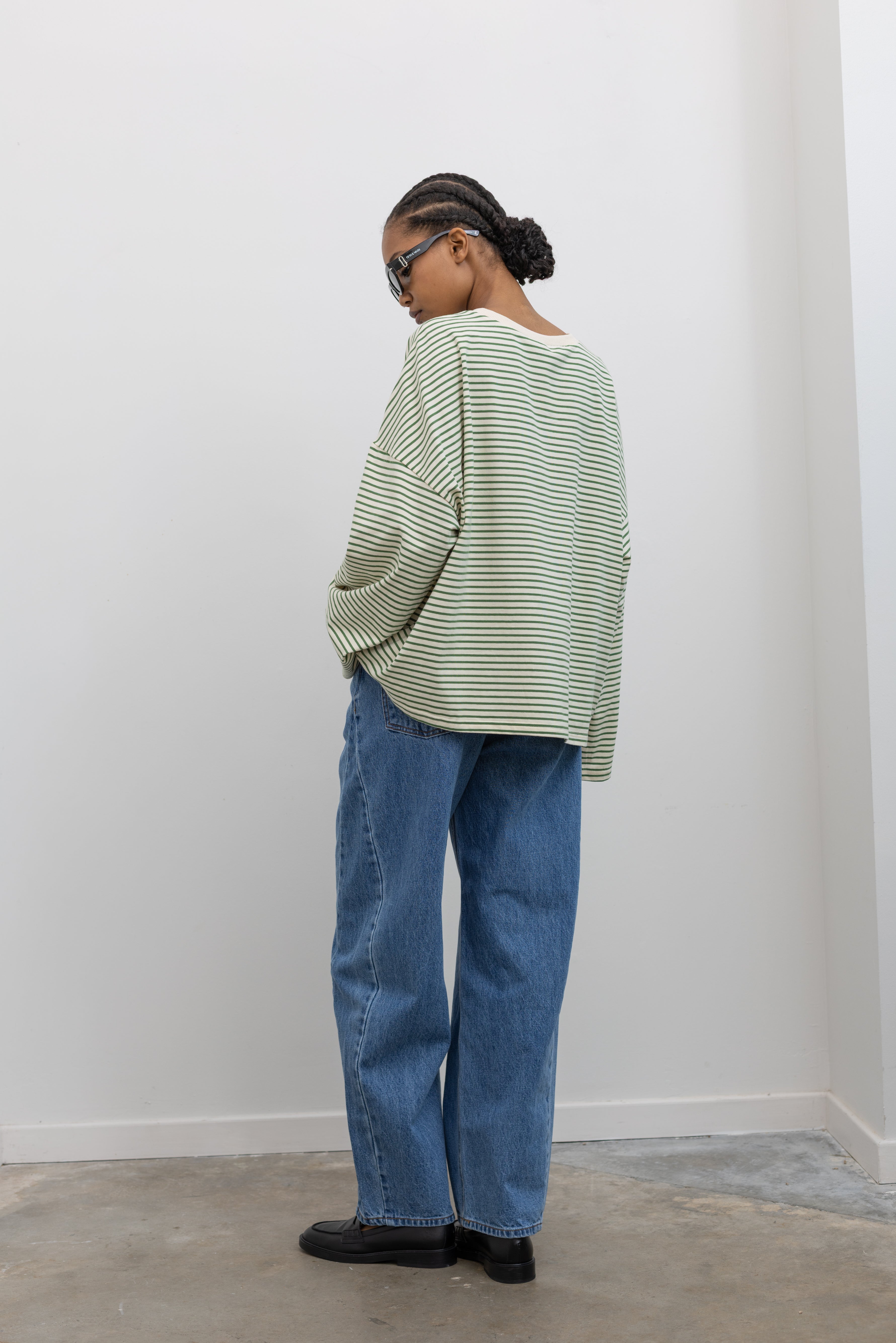 Full back view of a woman posing wearing Spring casual fashion in a Collective green and natural stripe dropped shoulder long sleeve cotton  oversized top paired with light wash denim at Alas Eius.