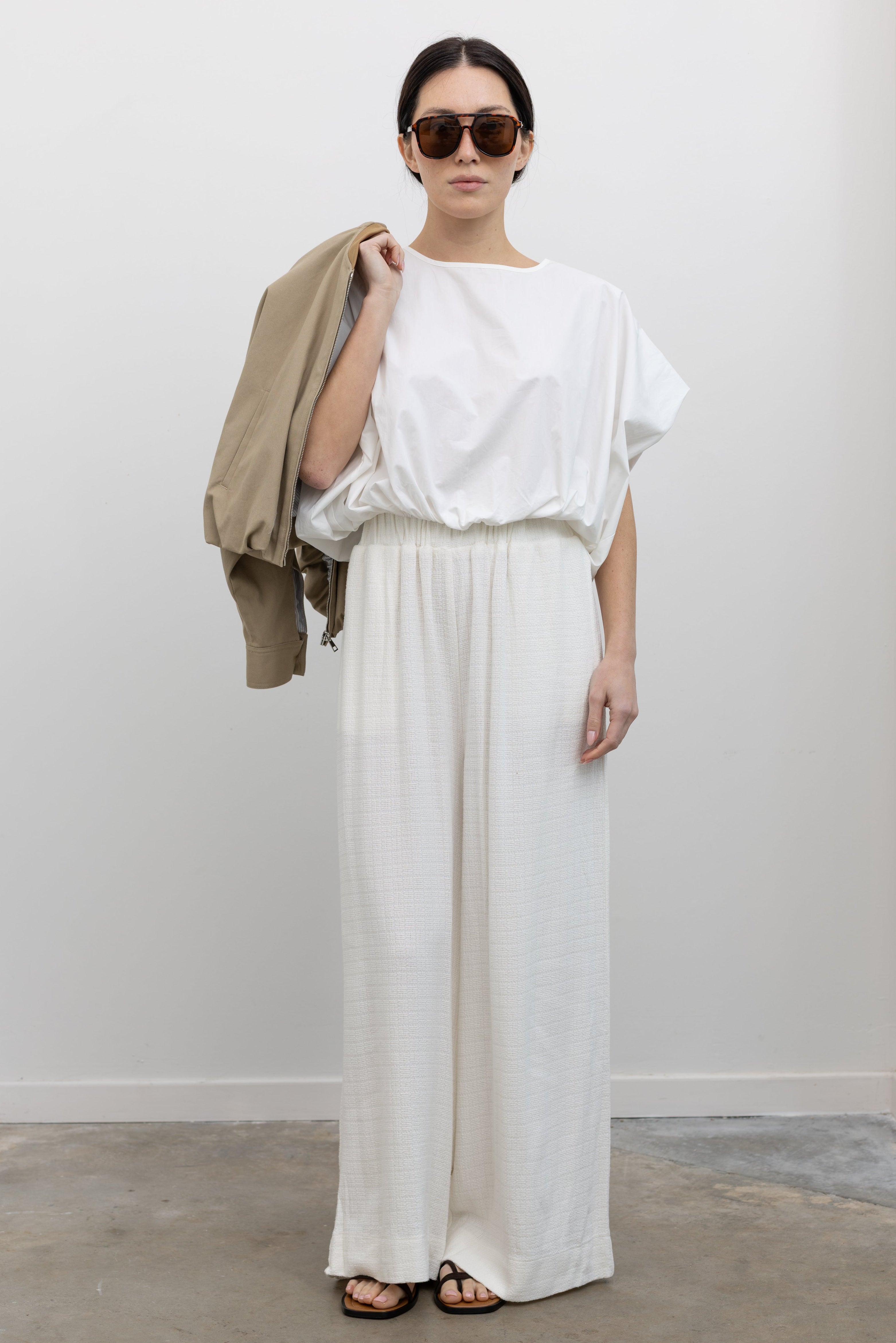 Full length front view of a woman wearing chic spring fashion in Collective Ivory Linen Wide Leg Pants paired with an oversized short sleeve top and strappy leather sandals at Alas Eius.