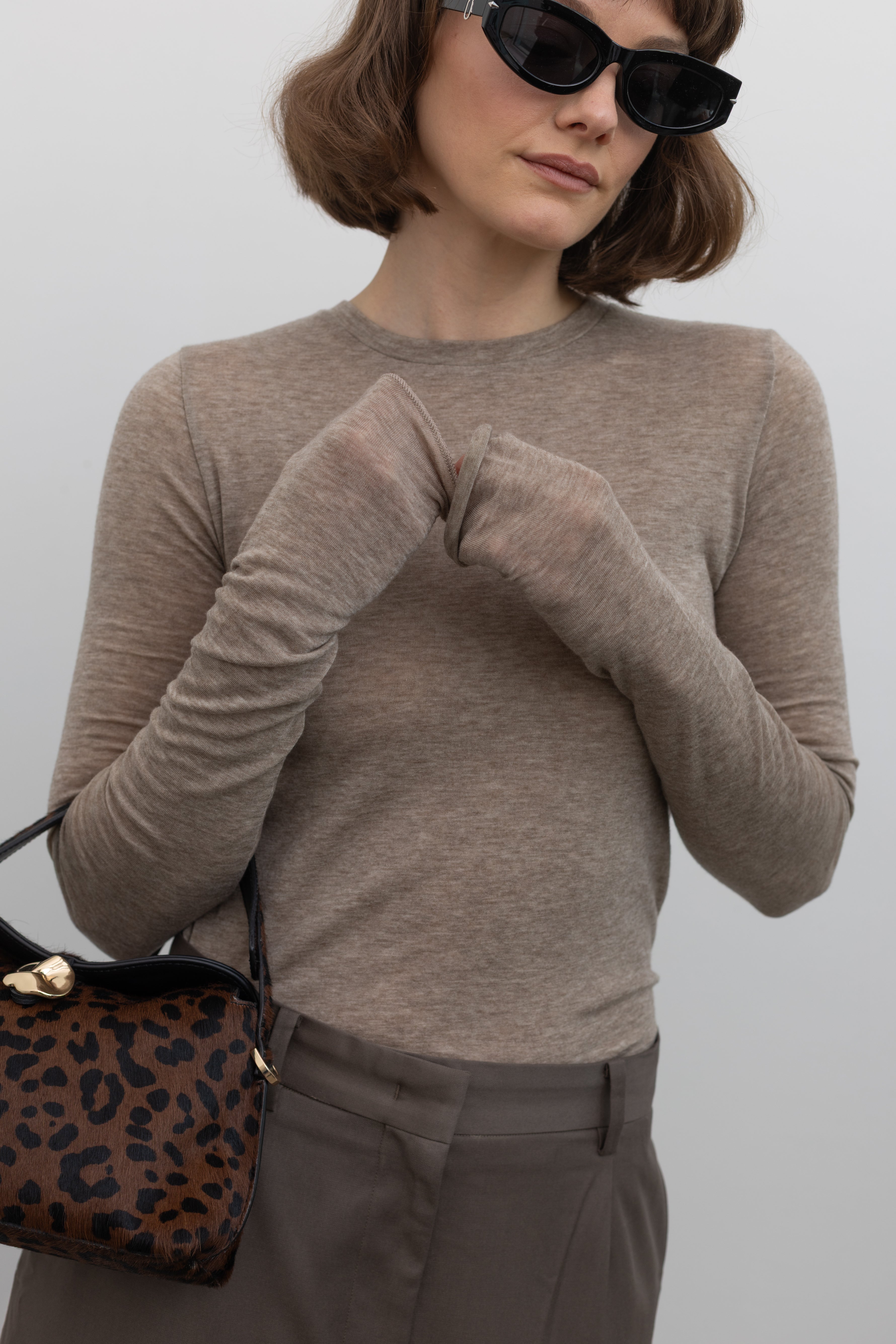 Close-up front view of a woman wearing an elevated capsule wardrobe essential in a Collective Brand Beige Merino Wool Long Sleeve Fitted Top at Alas Eius. 