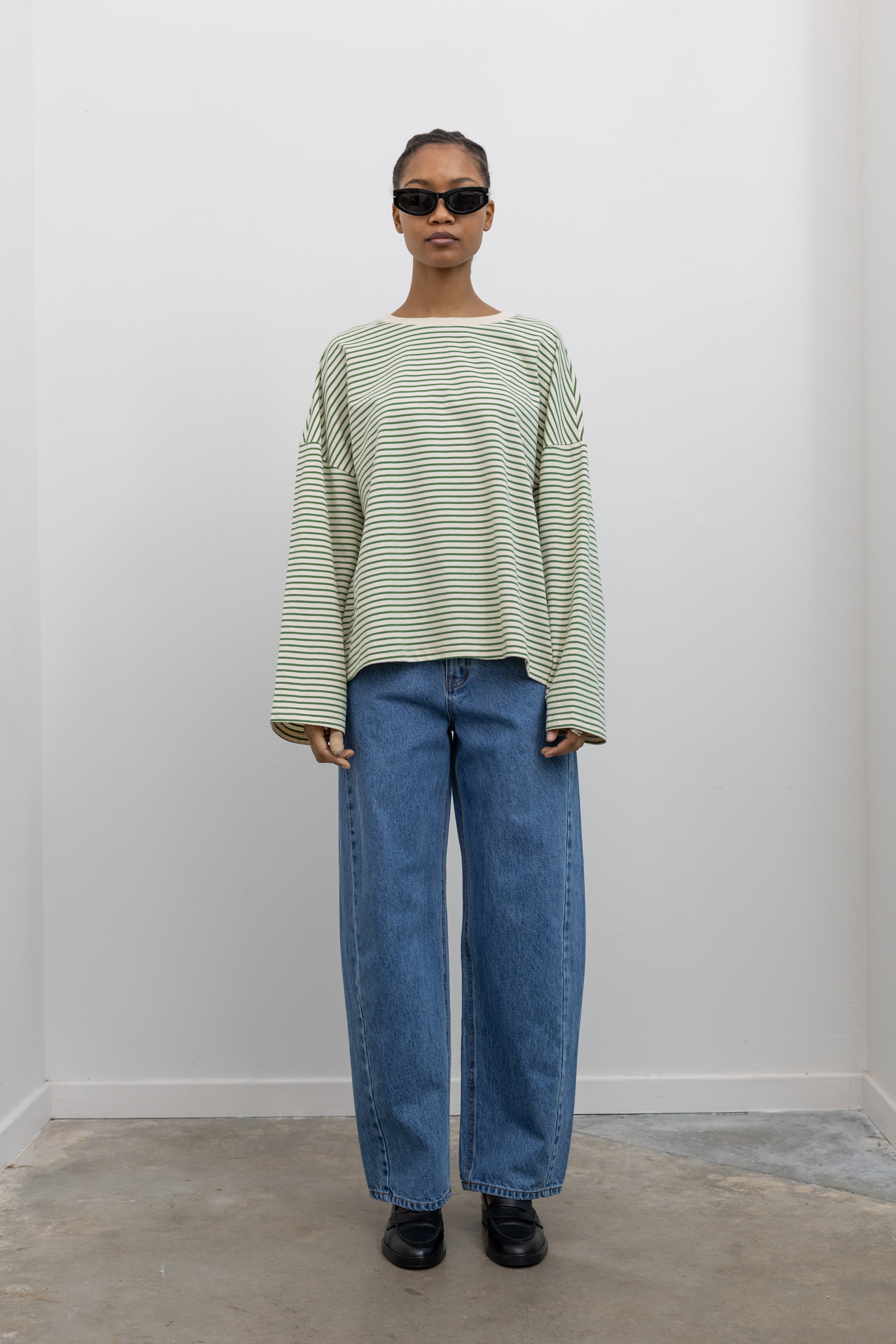 Full front view of a woman standing wearing Spring casual fashion in a Collective green and natural stripe dropped shoulder long sleeve cotton  oversized top paired with light wash denim at Alas Eius.