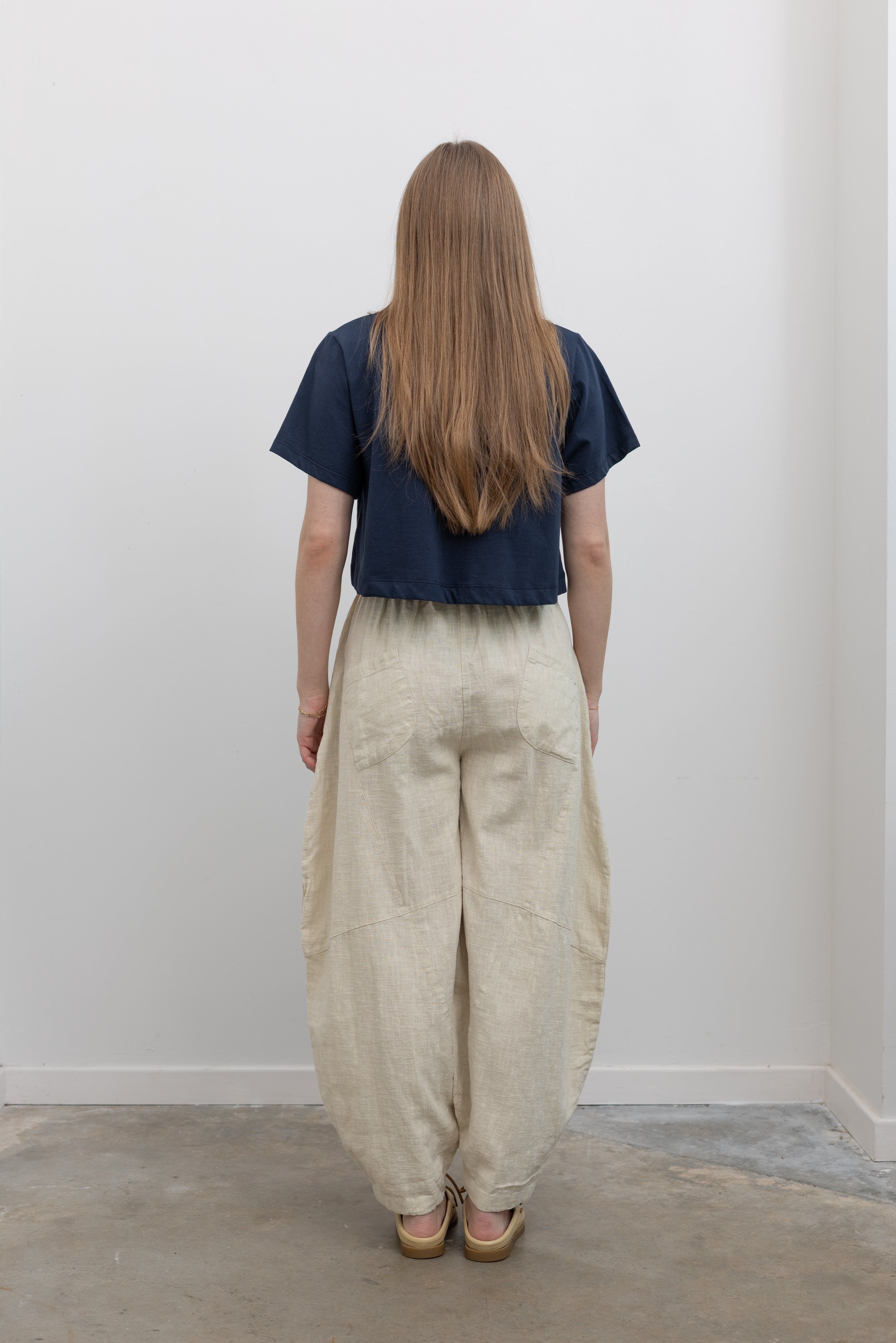 Back view of woman standing wearing Spring fashion in an Alas Eius label navy blue crop top with a pair of Collective Linen Barrel Cotton Blend Pants and leather mule shoes at Alas Eius 