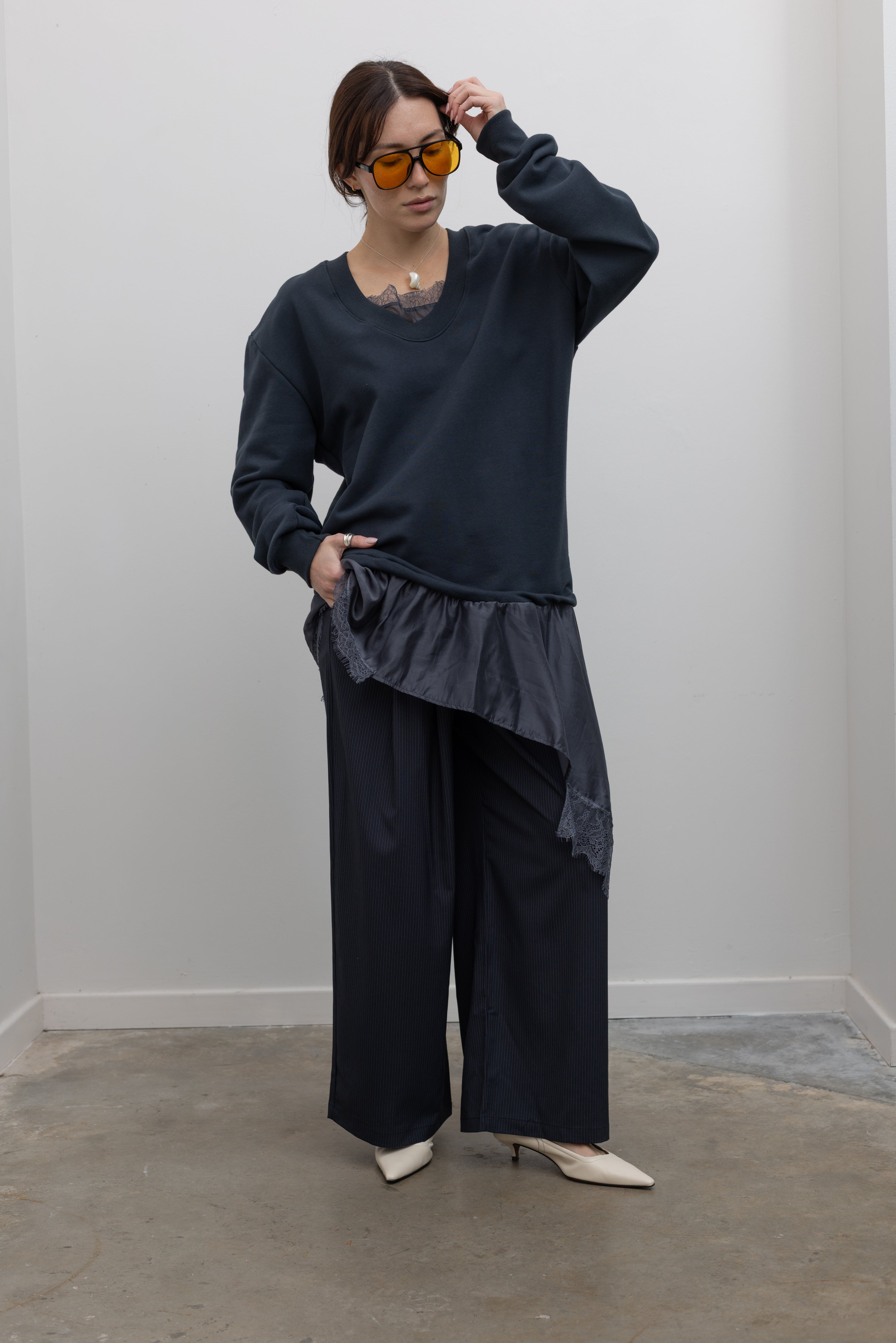 Woman standing wearing Spring fashion in a Collective Navy Lace Trim Cotton Oversized Jumper and navy blue pinstripe trousers with sunglasses and white pumps at Alas Eius 