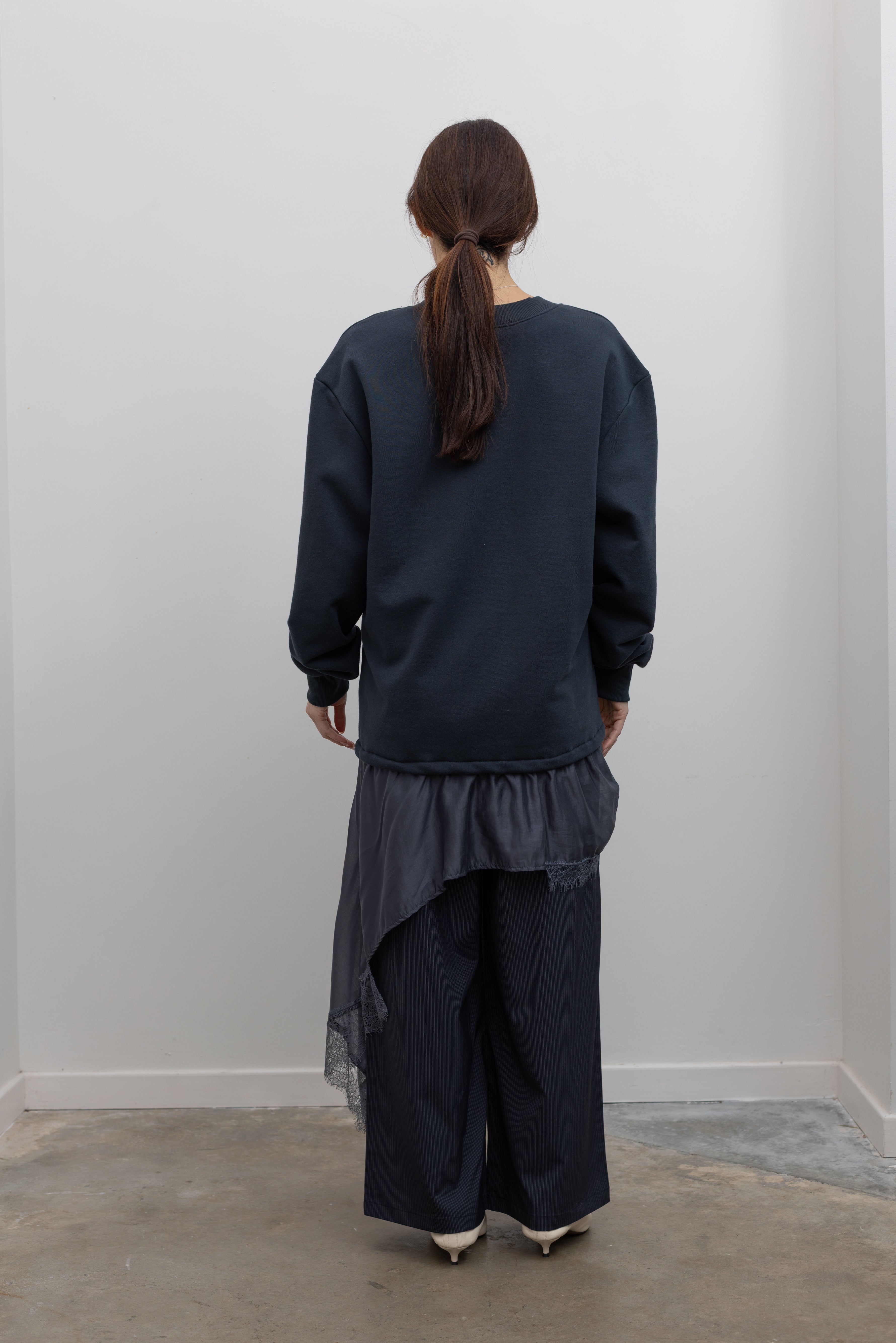 Back view of Woman standing wearing Spring fashion in a Collective Navy Lace Trim Cotton Oversized Jumper and navy blue pinstripe trousers with sunglasses and white pumps at Alas Eius 