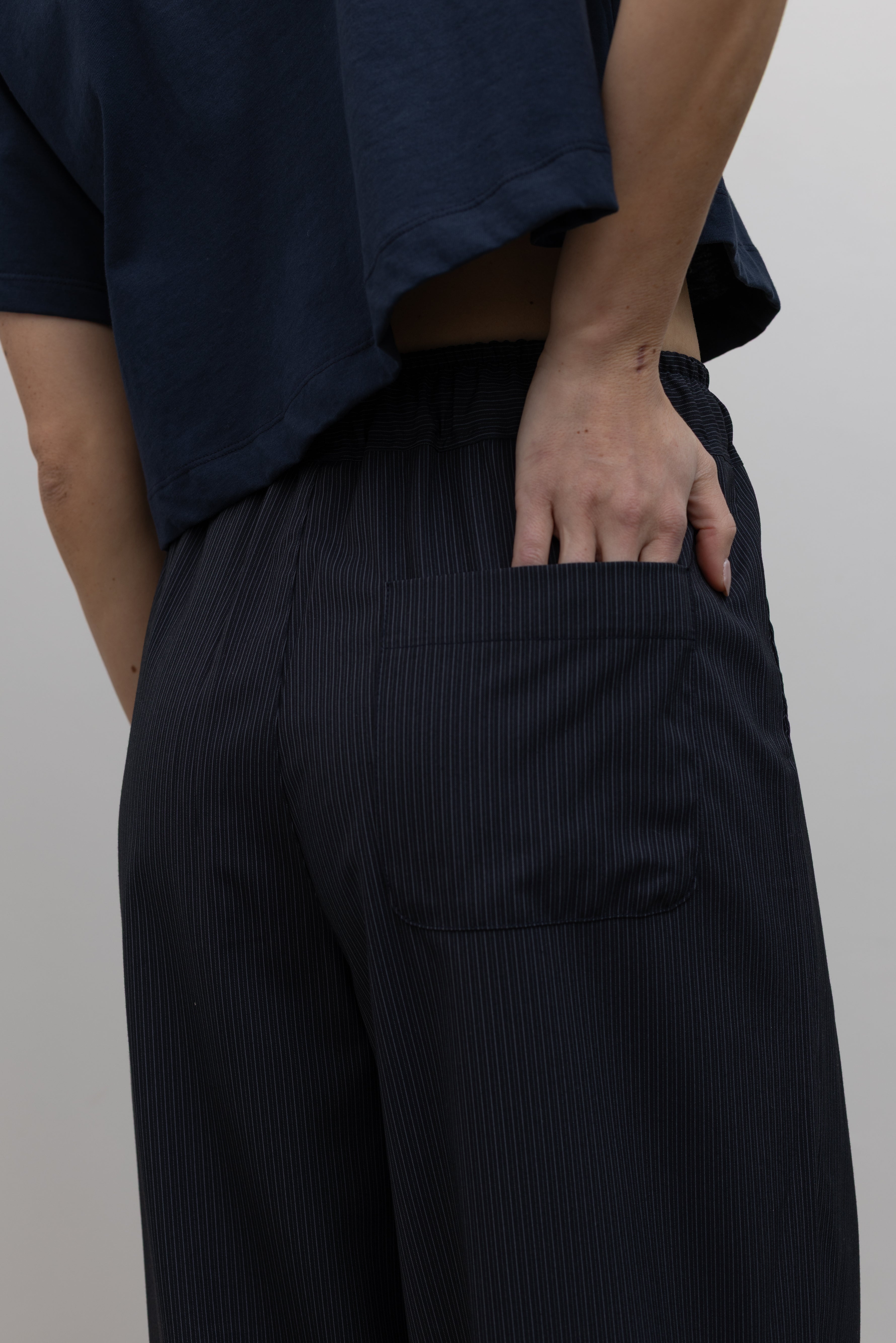 Detailed product view of Woman standing wearing Spring fashion in a pair of Collective Navy Pinstripe Wide Leg Drawstring Pants and navy blue tee with black beaded accessory at belt loop at Alas Eius
