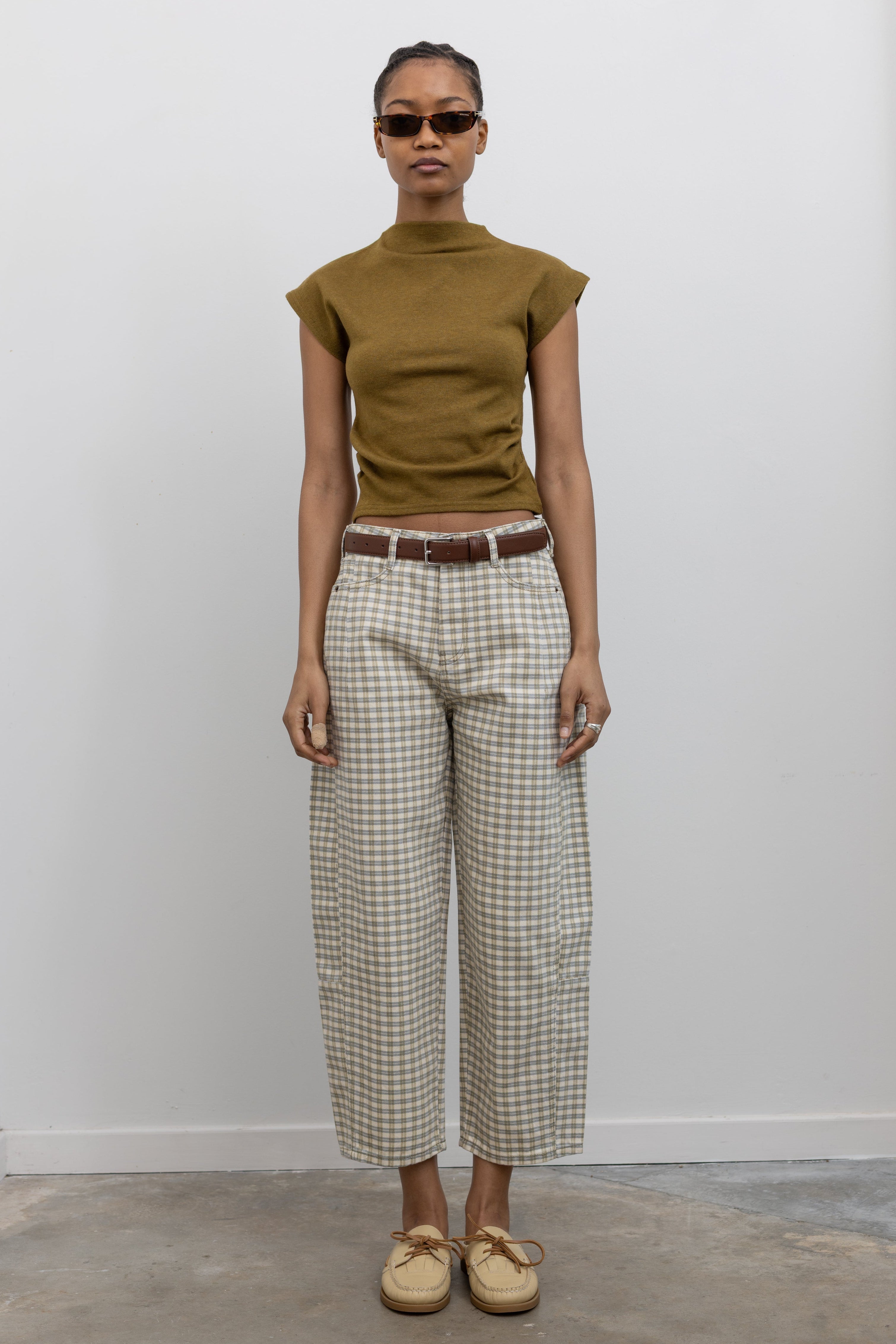 Front view of a woman standing wearing Spring fashion in a pair of Collective Olive Checkered Barrel Cropped Pants with a short sleeved top and beige leather shoes at Alas Eius