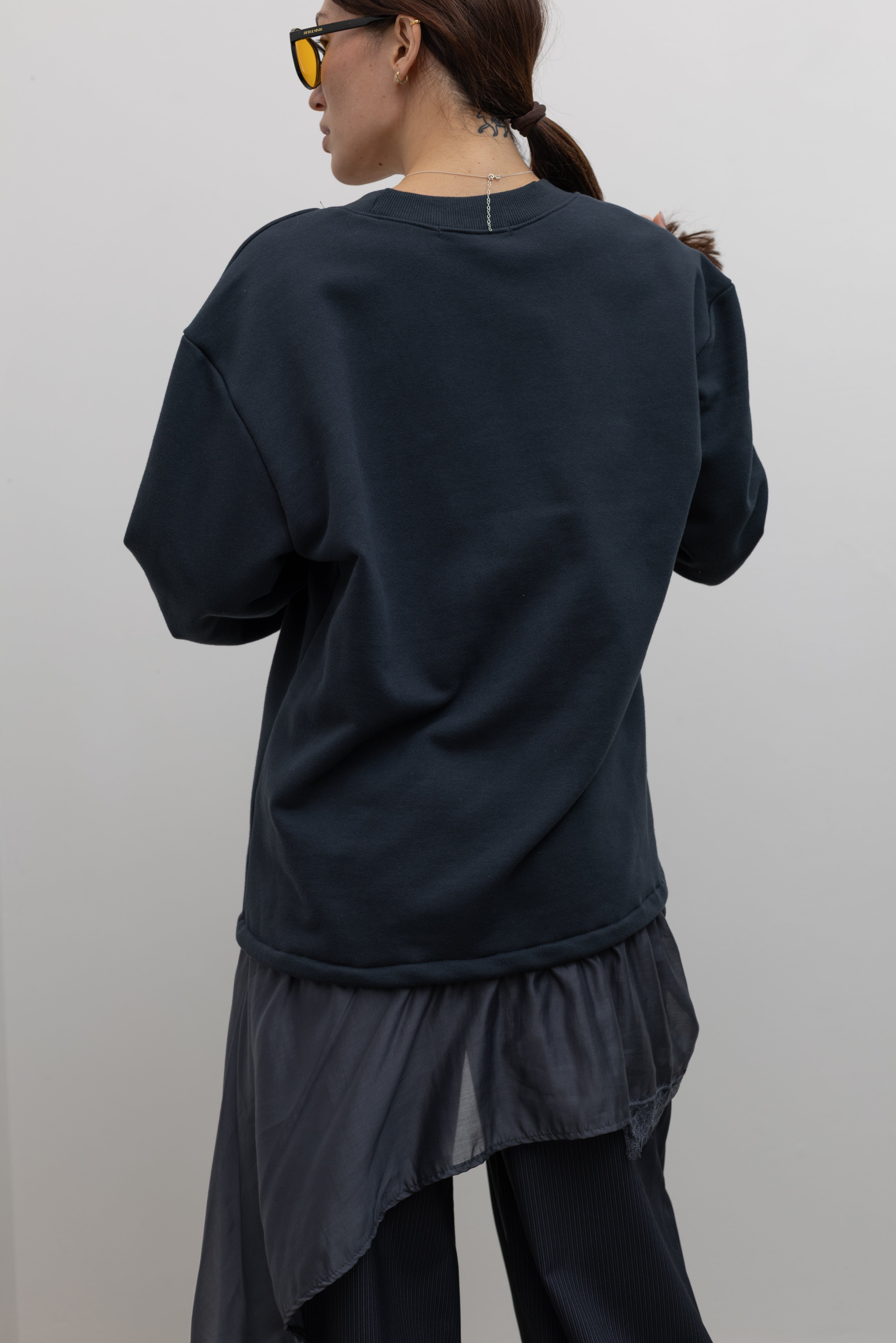 Back view of Woman standing wearing Spring fashion in a Collective Navy Lace Trim Cotton Oversized Jumper and navy blue pinstripe trousers with sunglasses and white pumps at Alas Eius 