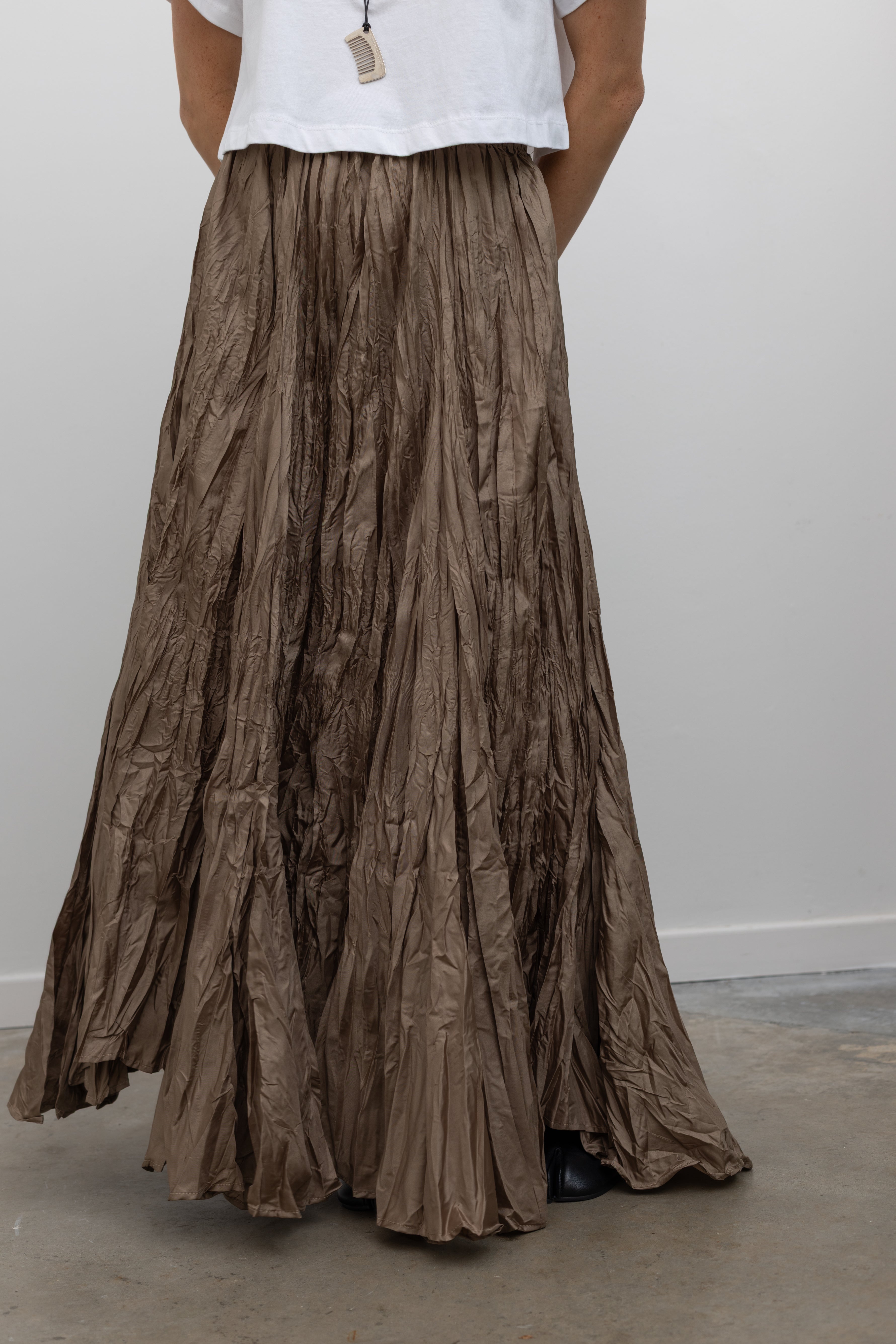 Close-up front view of a woman wearing contemporary spring fashion in an Alas Eius label cropped white t-shirt paired with a Collective Khaki Crinkle Textured Maxi Skirt at Alas Eius. 