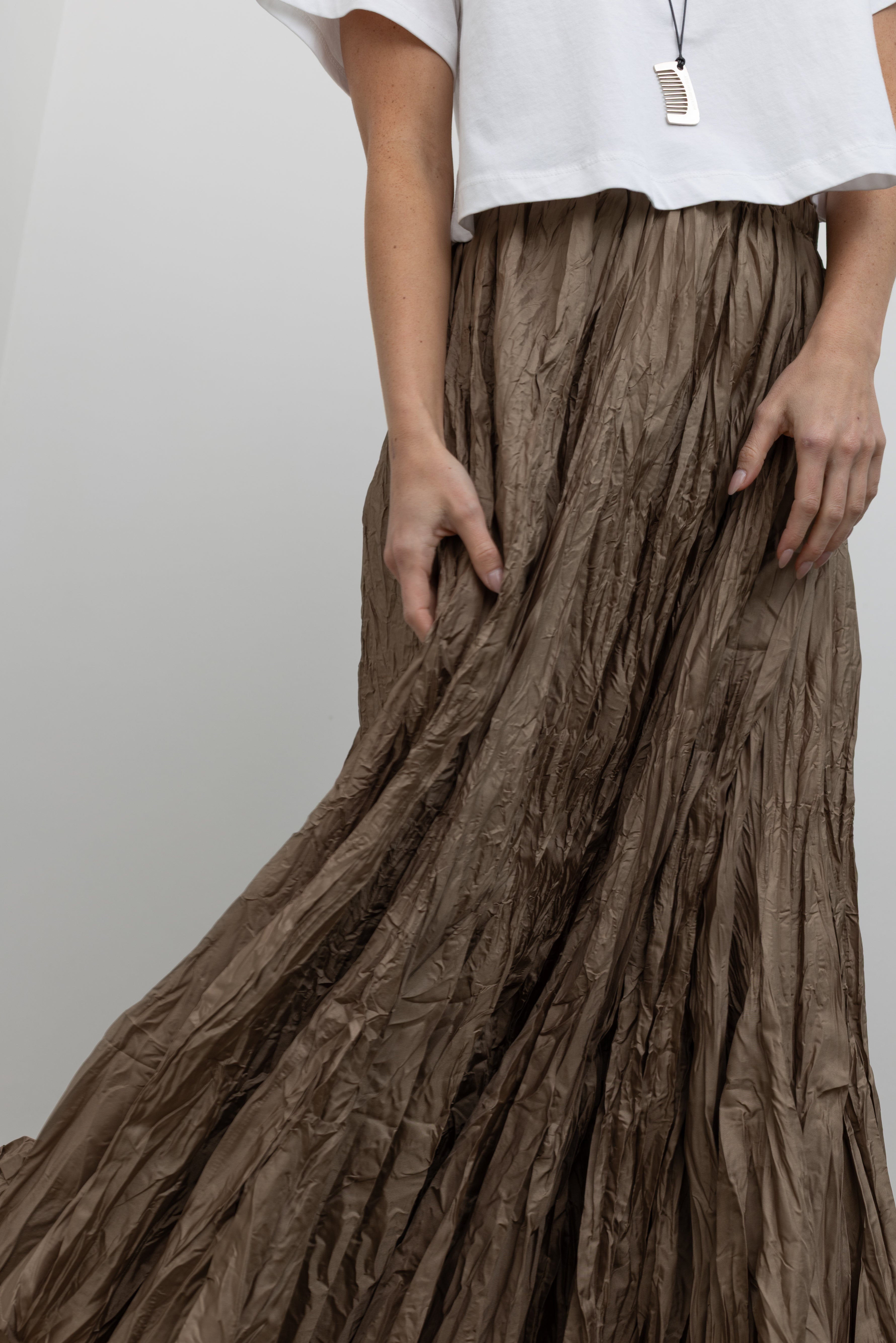 Close-up front view of a woman wearing contemporary spring fashion in an Alas Eius label cropped white t-shirt paired with a Collective Khaki Crinkle Textured Maxi Skirt at Alas Eius. 