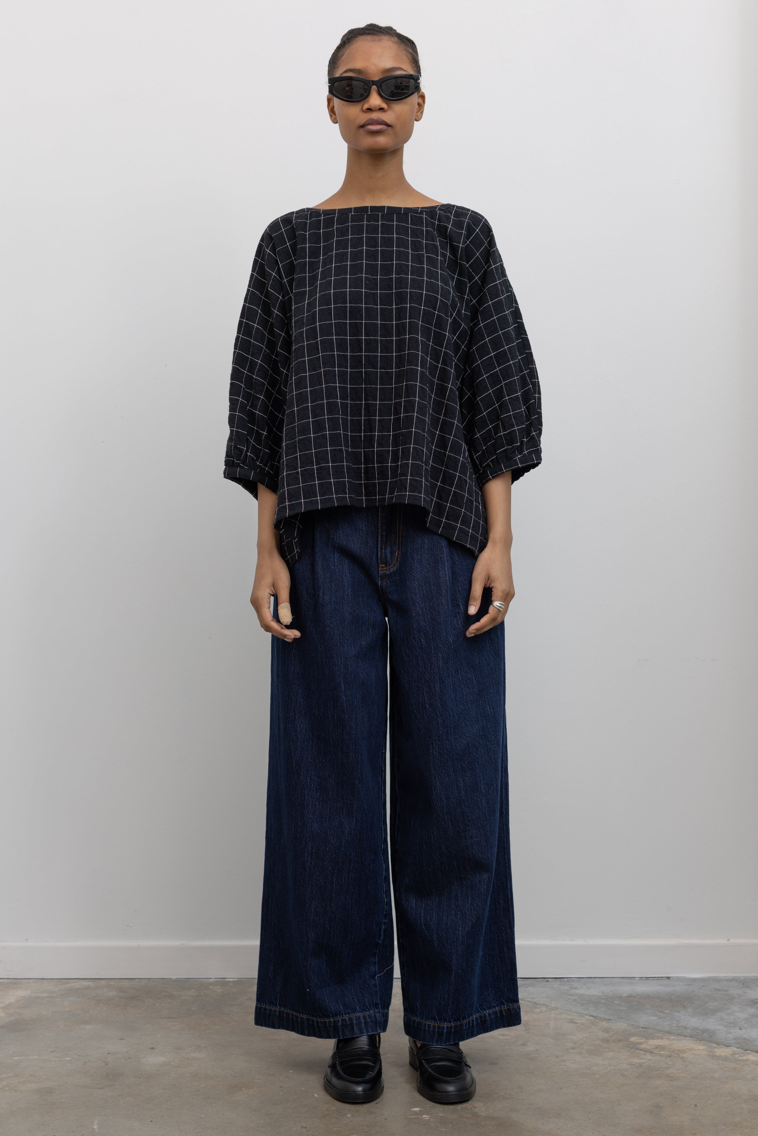 Full front view of a woman wearing a classic wardrobe staple in a pair of Collective indigo denim wide leg pleated jeans with a black top and black leather loafers at Alas Eius.