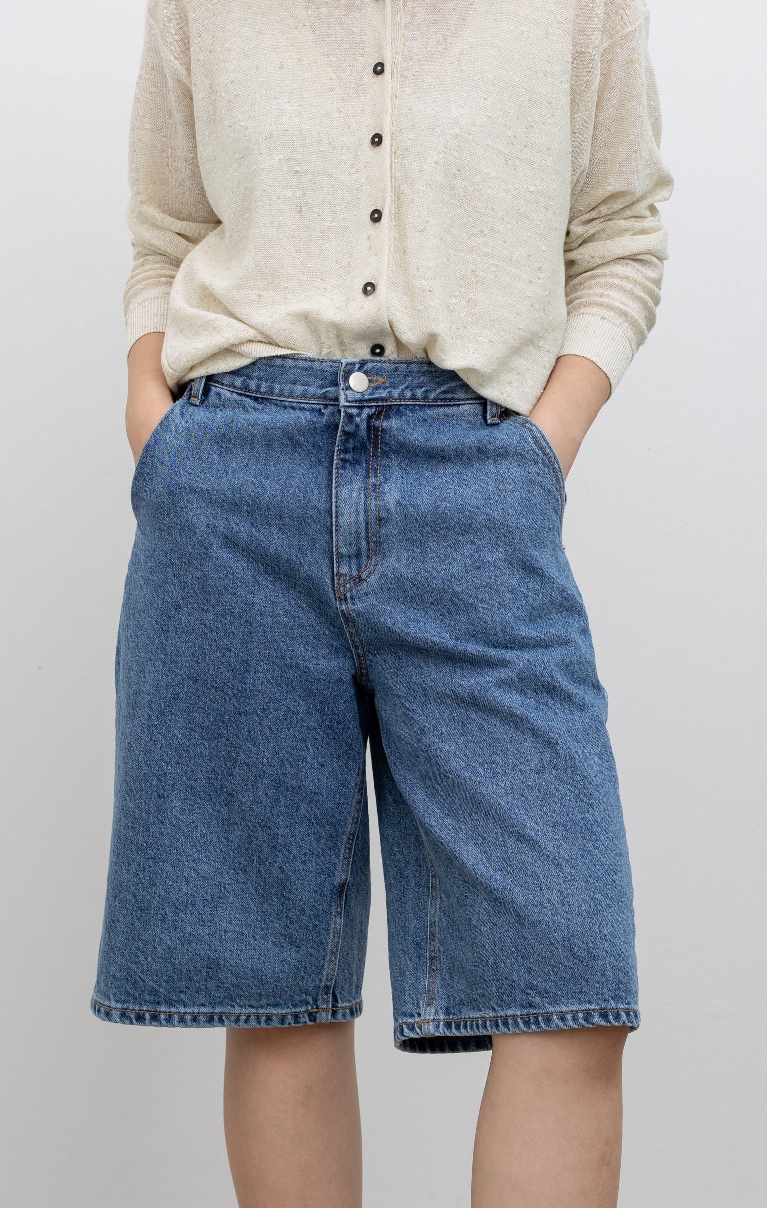 Model wearing summer fashion in the Collective Stone-washed bermuda denim shorts with a mid-to-high rise, relaxed thigh fit, wide-leg silhouette, and knee-length design at Alas Eius.