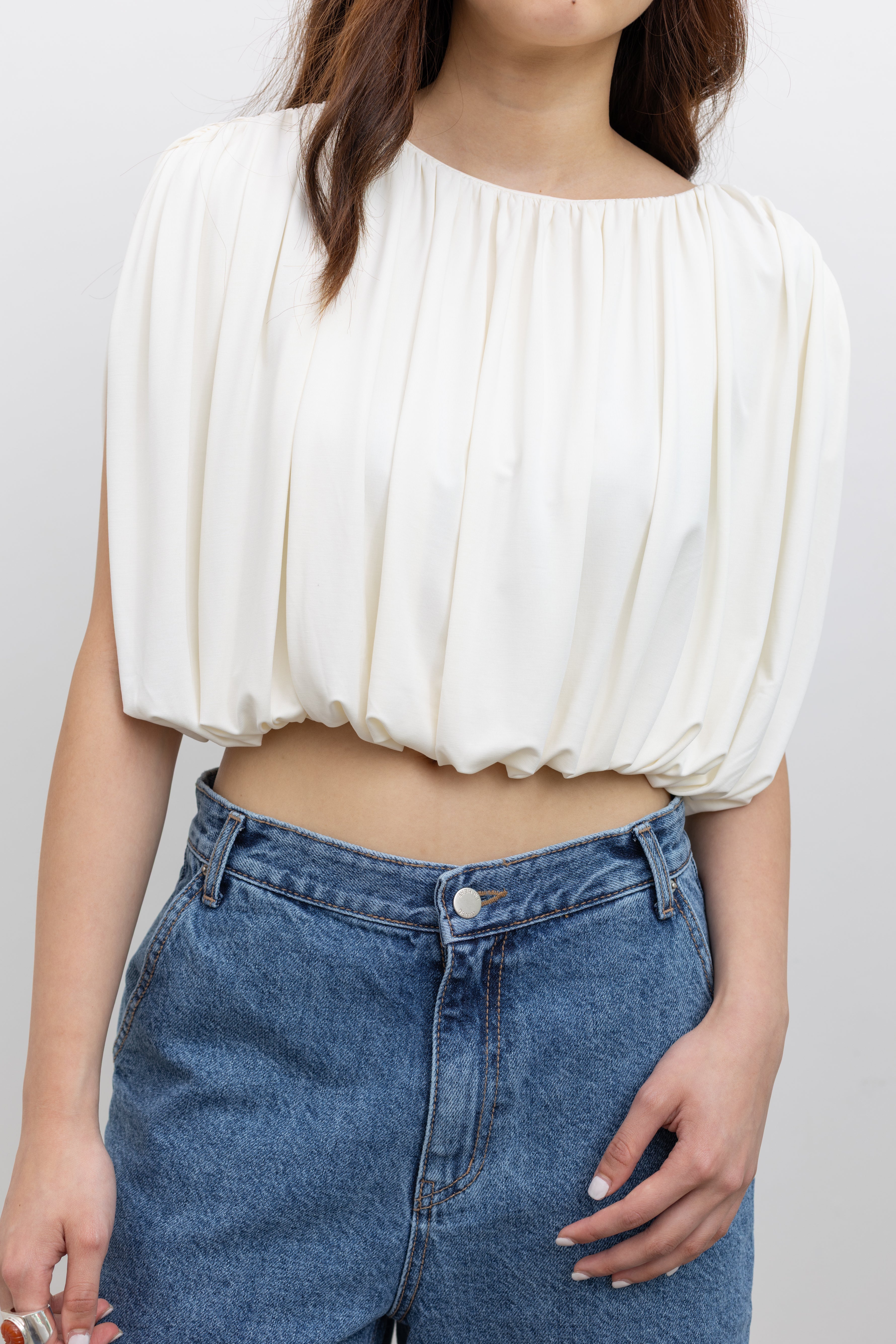Model wearing chic summer fashion in a Collective white pleated balloon top with all-over gathering, a voluminous puff cropped hem, and a fully lined relaxed silhouette paired with stone washed bermuda shorts at Alas Eius. 