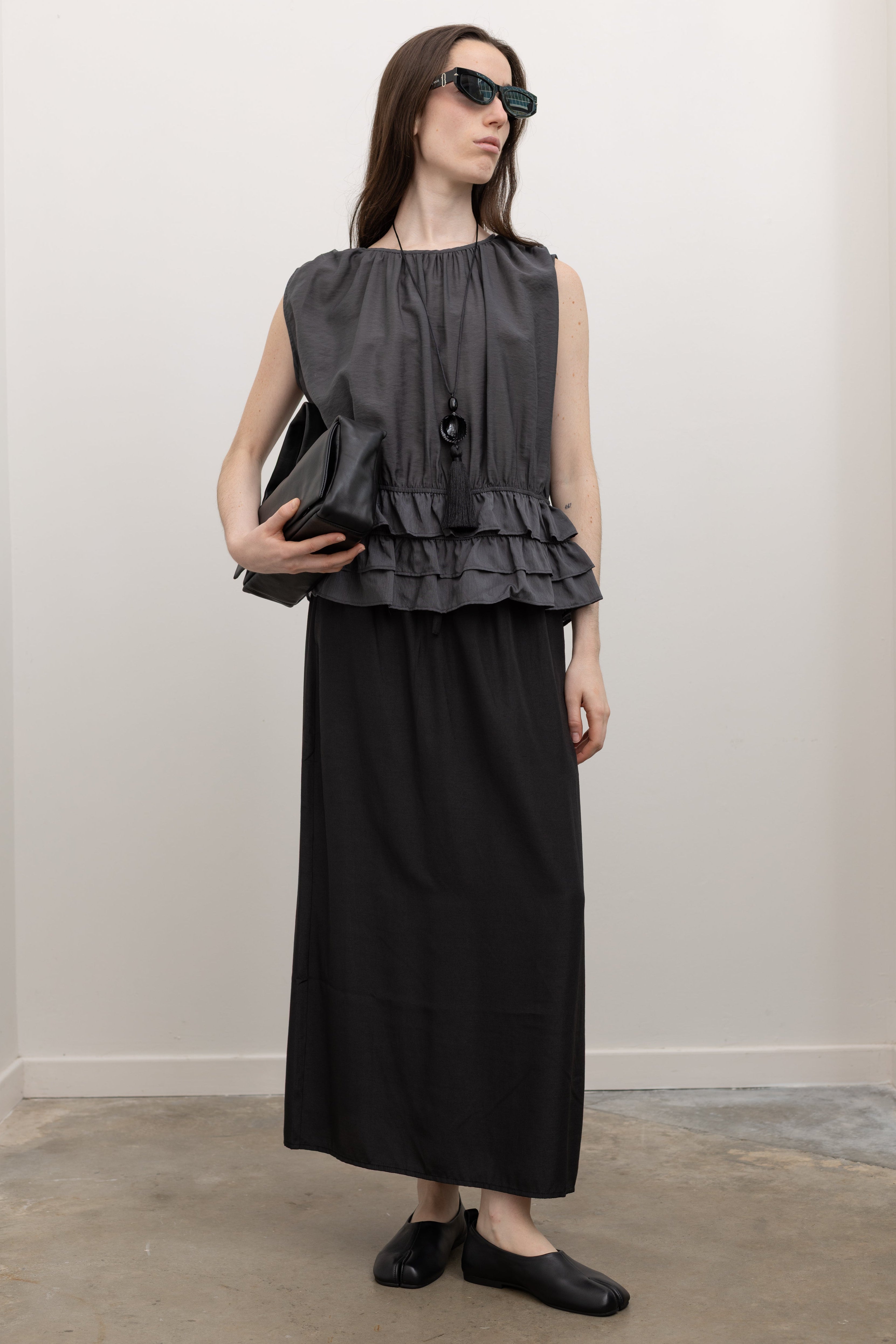 Collective fluid sleeveless blouse in charcoal Tencel featuring shirred waist detailing, soft gathered neckline, and tiered ruffle hem for elegant evening wear styling at Alas Eius