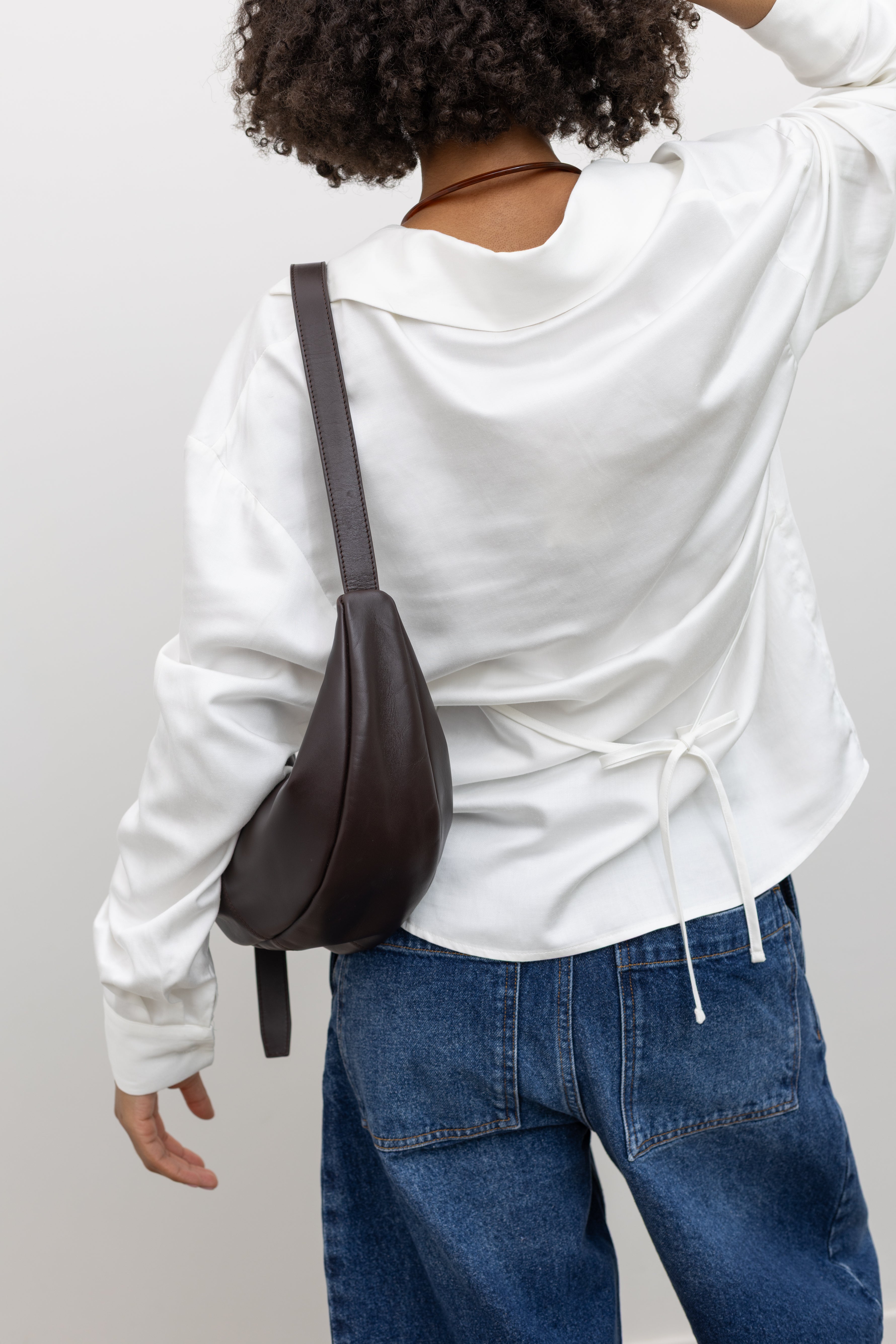 Woman wearing a versatile capsule wardrobe staple in a Collective lightweight white cotton gathered blouse with long sleeves, a relaxed fit, and front tie detail, and deep v neckline paired with blue denim jeans at Alas Eius. 