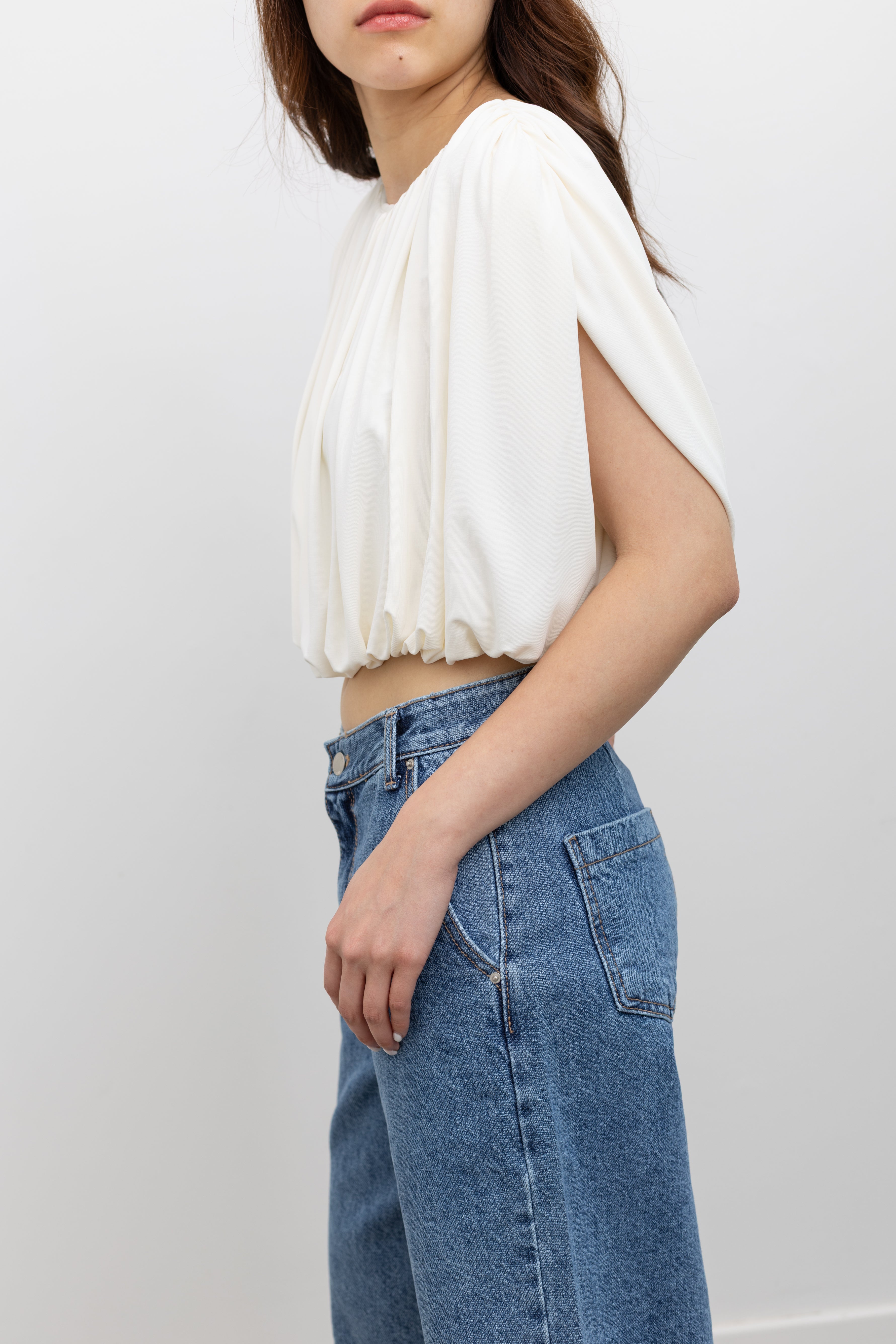 Model wearing chic summer fashion in a Collective white pleated balloon top with all-over gathering, a voluminous puff hem, and a fully lined relaxed silhouette paired with stone washed bermuda shorts at Alas Eius. 