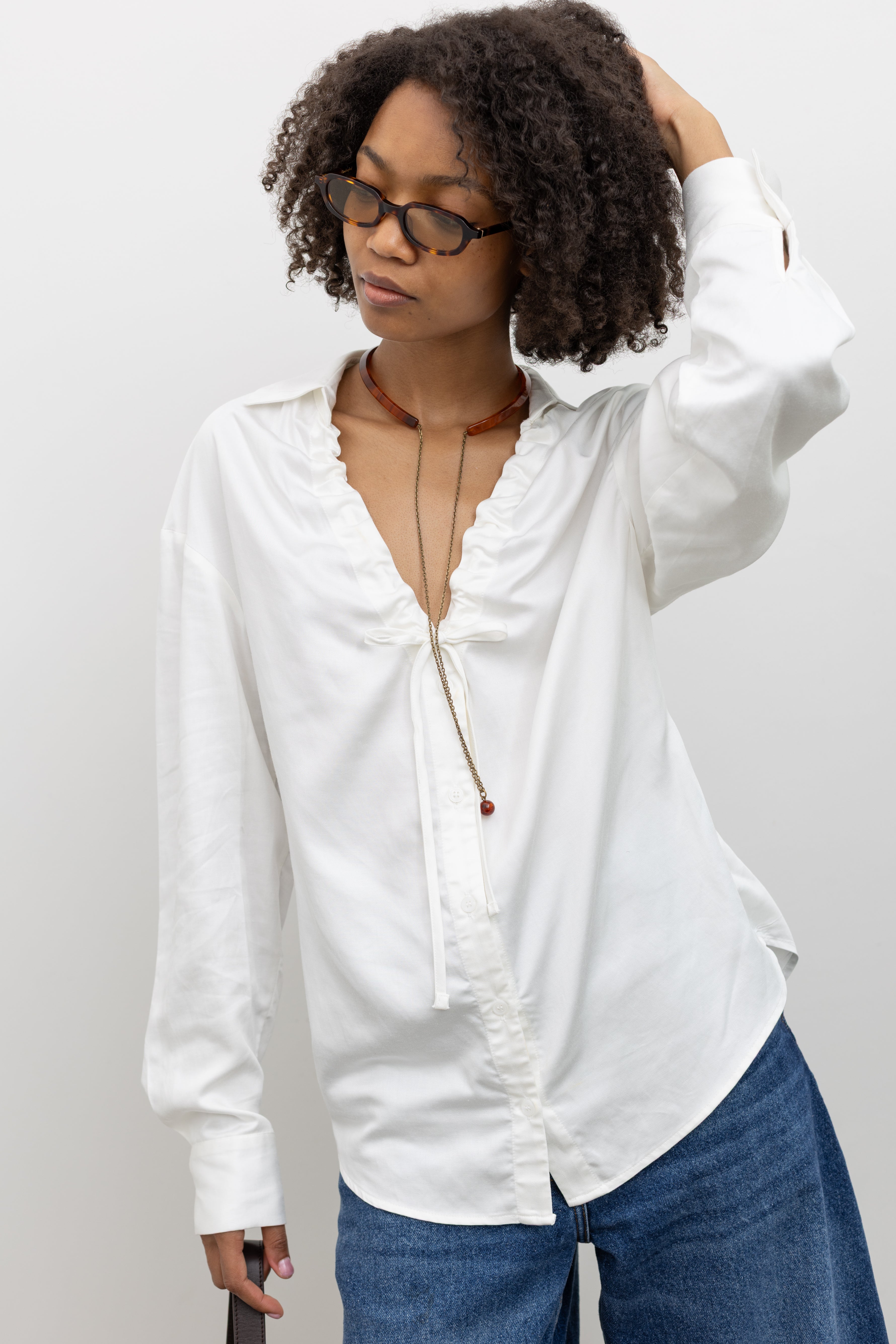 Woman wearing chic and contemporary fashion in a Collective lightweight white cotton gathered blouse with long sleeves, a relaxed fit, and front tie detail, paired with Rachel Comey Sculptural Back-Detail Statement Choker at Alas Eius. 