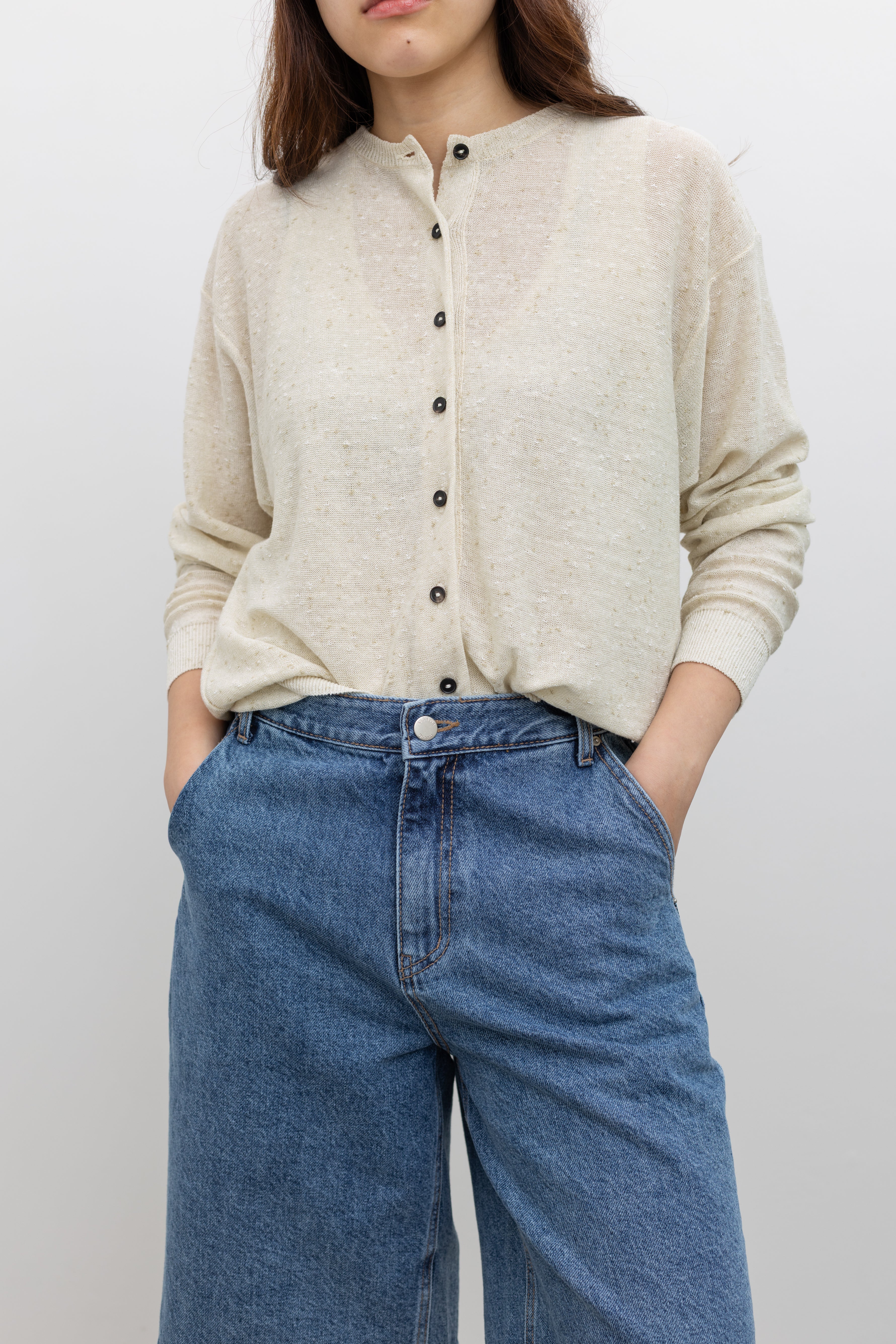 Woman wearing a cream flecked oversized cardigan by Cordera with a crew neckline, front button closure, and ribbed trim details in a relaxed linen and cotton blend silhouette at Alas Eius. 