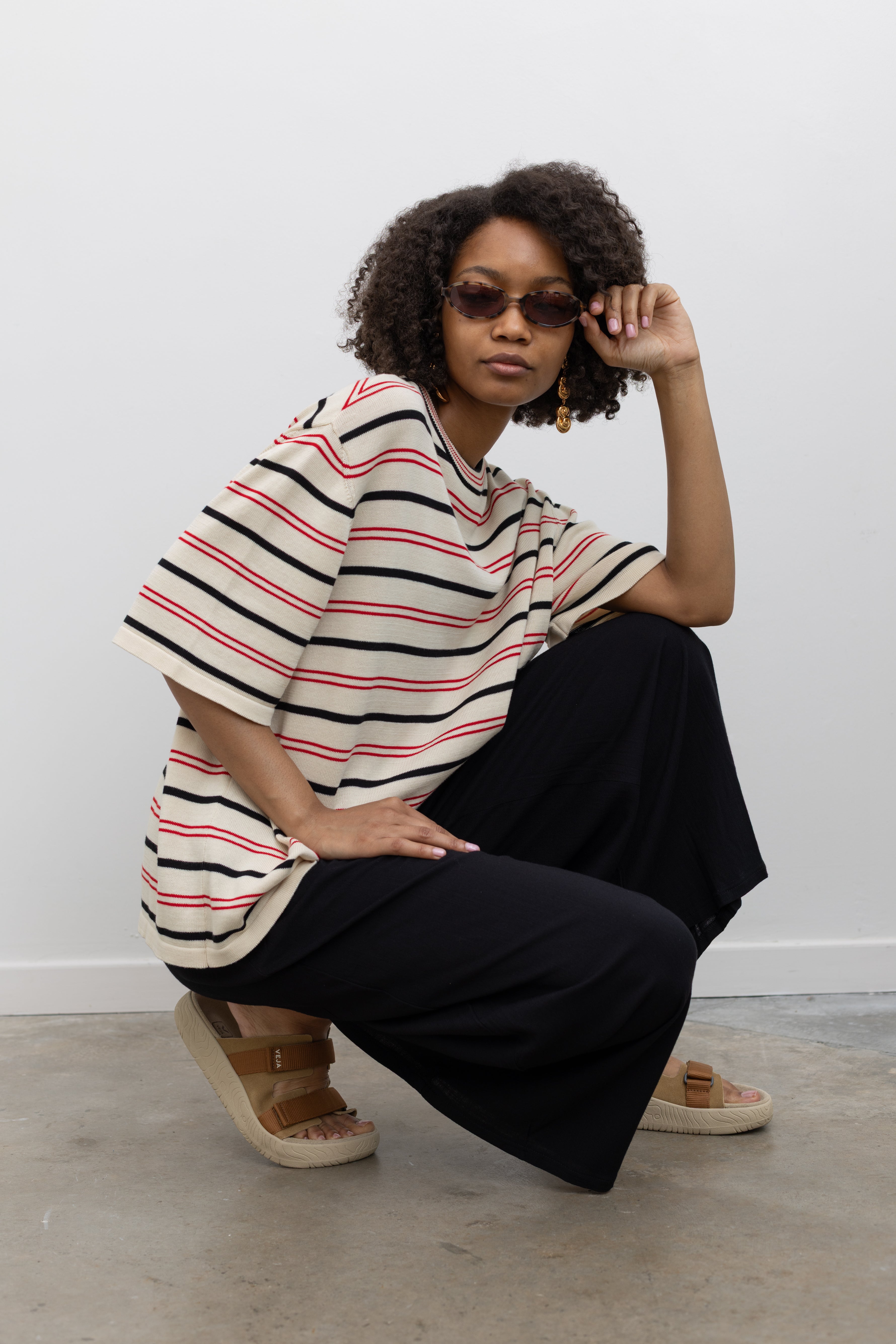 Model wearing capsule wardrobe fashion in a Coreda oversized t-shirt featuring a classic crew neck, red and black stripes in varying widths on an ecru background at Alas Eius.