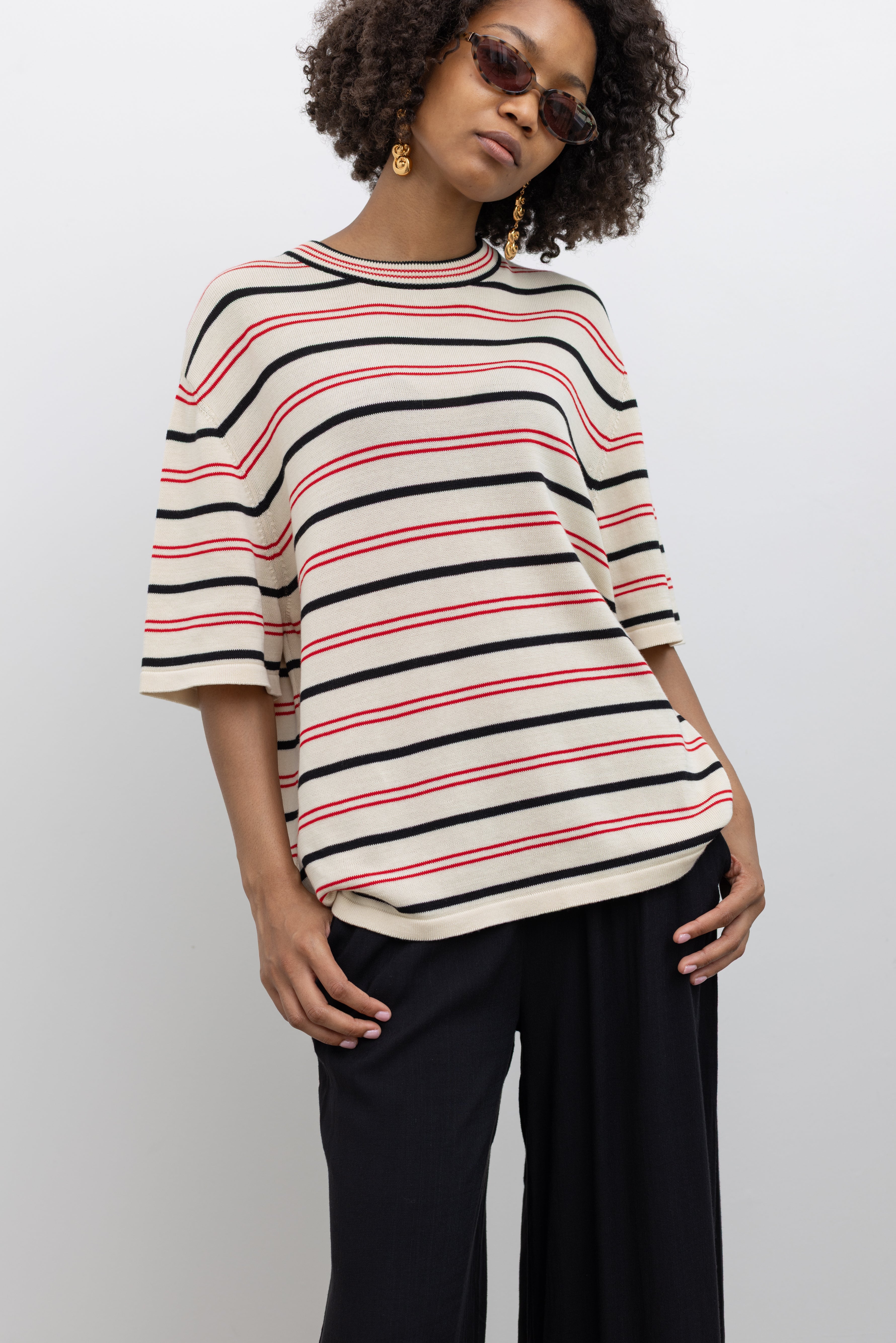Model wearing a Coreda oversized t-shirt featuring a classic crew neck, red and black stripes in varying widths on an ecru background at Alas Eius.