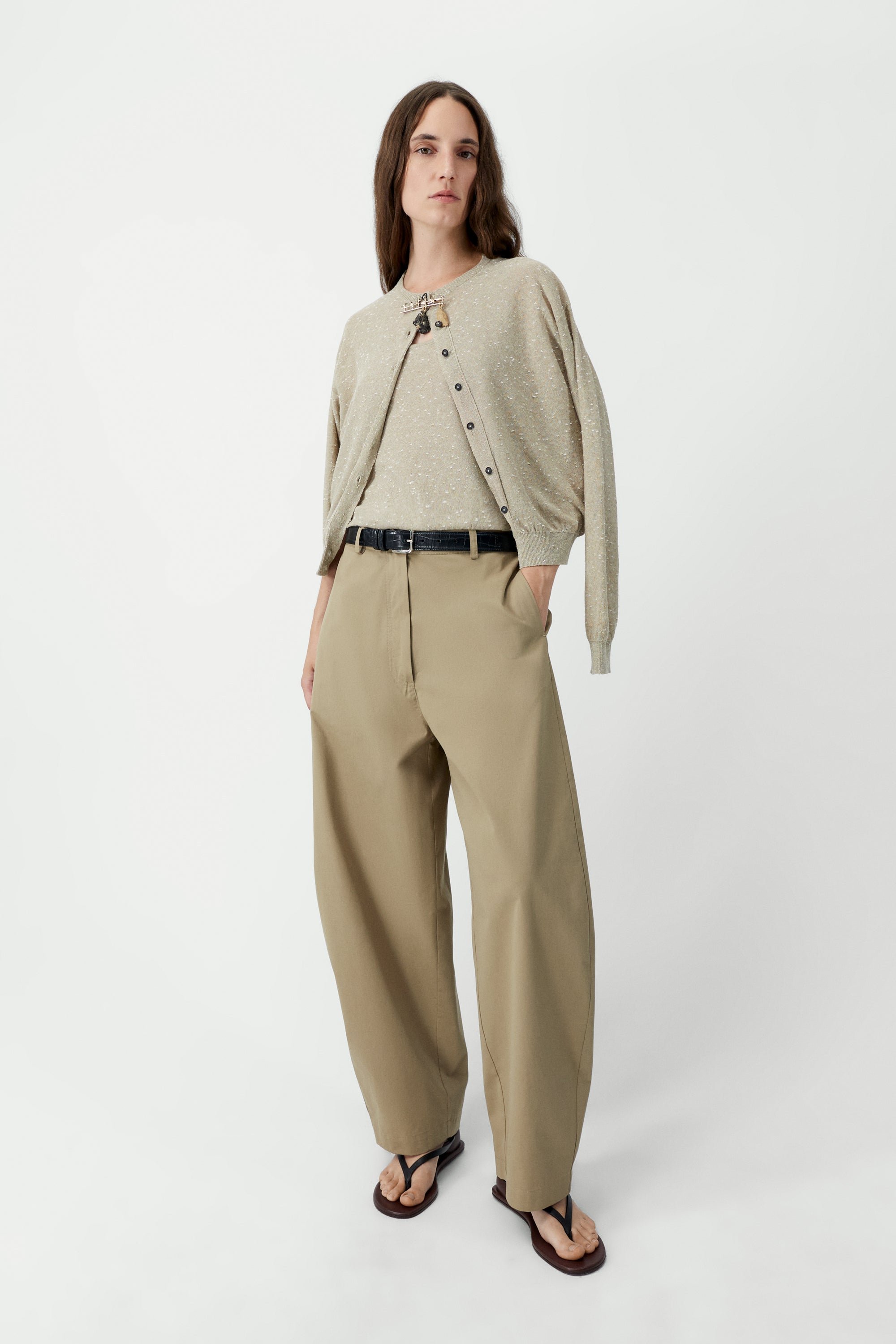 Full length front view of a woman standing wearing an elevated classic wardrobe staple in the Cordera beige linen and cotton blend flecked oversized cardigan featuring a crew neck and finished with ribbed trims at the collar, hem, and cuffs, it fastens with small front buttons at Alas Eius.  

This cardigan is ethically and carefully manufactured in La Coruña, with Japanese knitting machines and finished by hand.