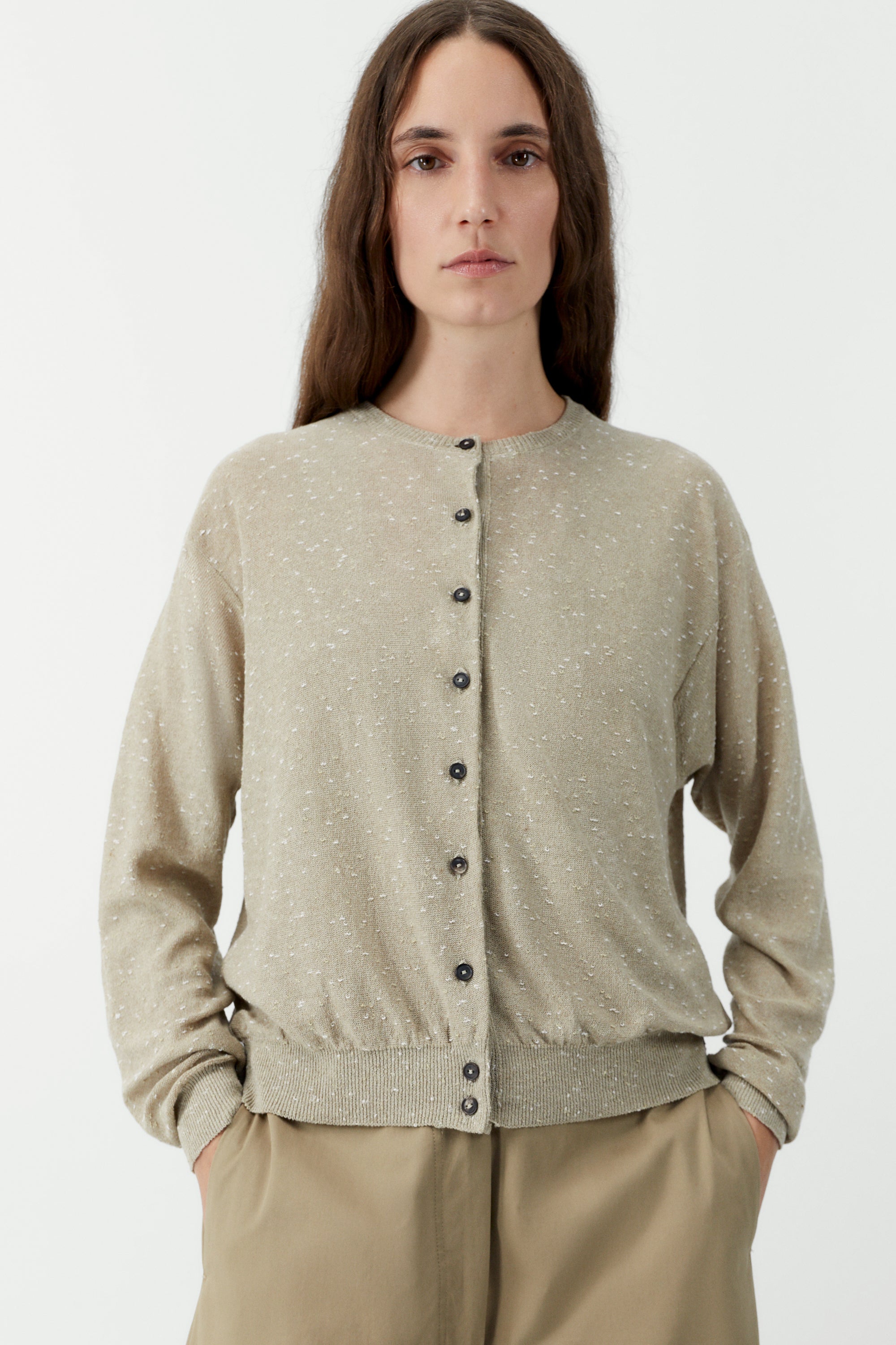 Front view of a woman standing wearing an elevated classic wardrobe staple in the Cordera cream linen and cotton blend flecked oversized cardigan featuring a crew neck and finished with ribbed trims at the collar, hem, and cuffs, it fastens with small front buttons at Alas Eius.  

This cardigan is ethically and carefully manufactured in La Coruña, with Japanese knitting machines and finished by hand.