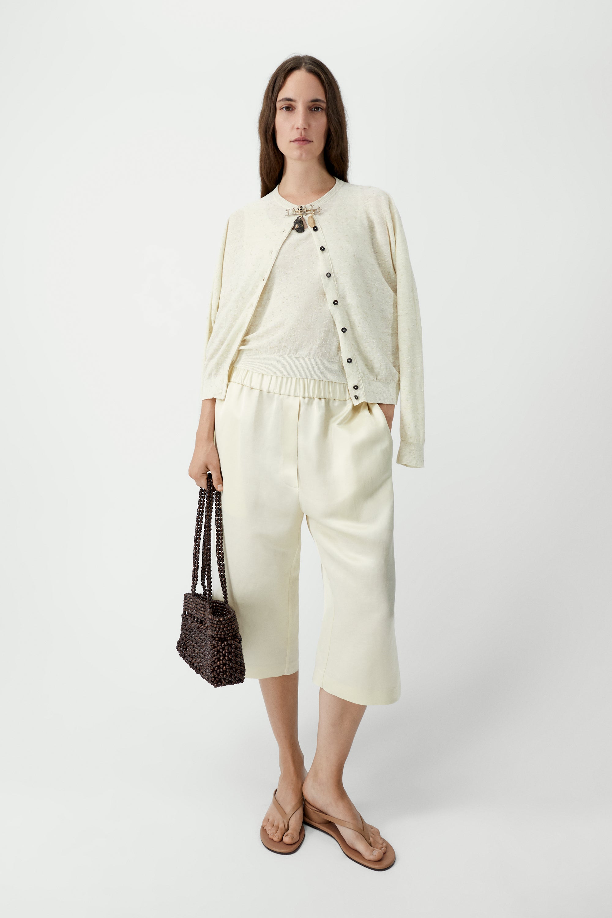 Full length front view of a woman standing wearing an elevated classic wardrobe staple in the Cordera cream linen and cotton blend flecked oversized cardigan featuring a crew neck and finished with ribbed trims at the collar, hem, and cuffs, it fastens with small front buttons at Alas Eius.  

This cardigan is ethically and carefully manufactured in La Coruña, with Japanese knitting machines and finished by hand.

