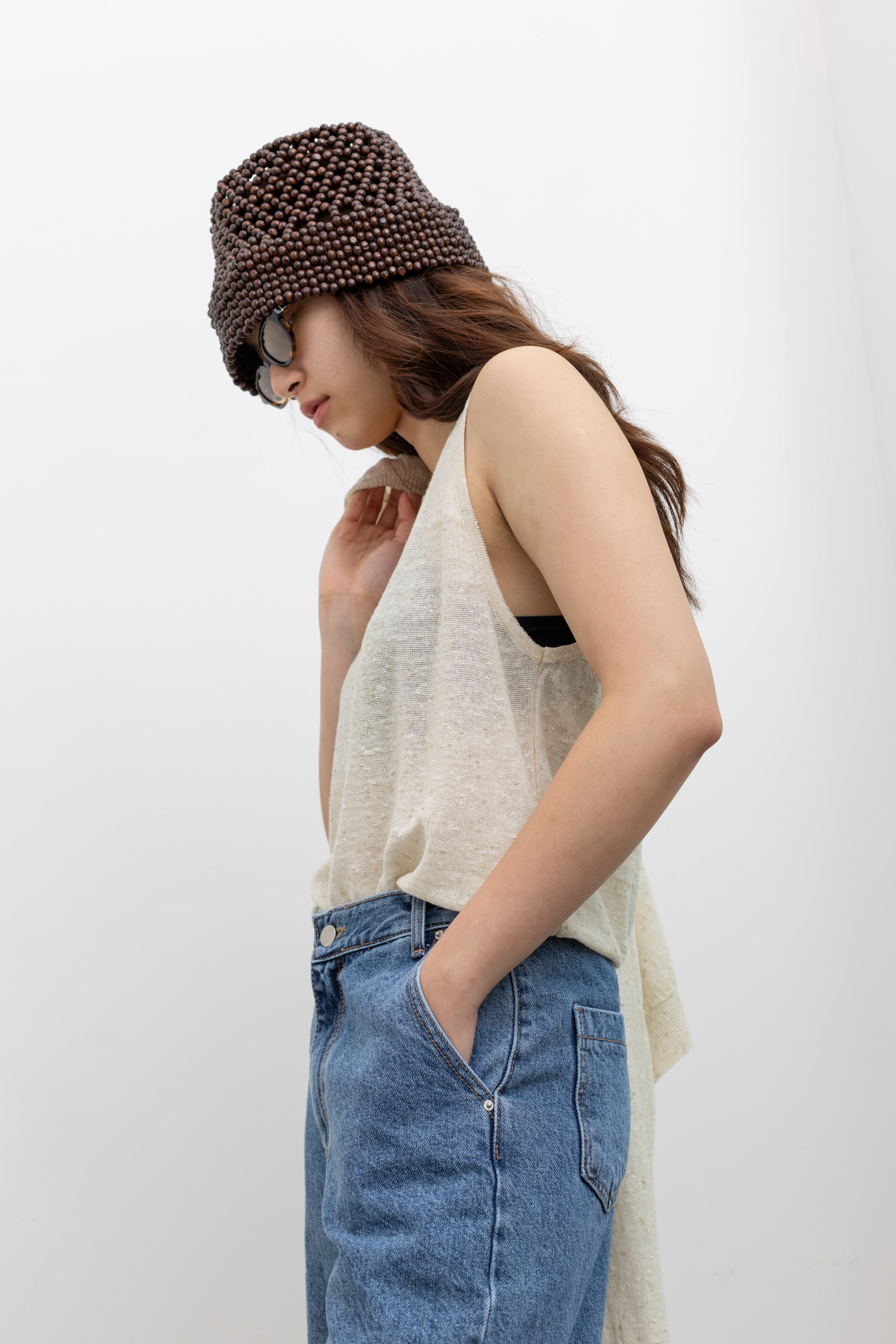 Model wearing natural fiber outfit in a Cordera elevated cream oversized tank featuring a soft draped fit and lightweight summer-ready fabric with cotton denim bermuda shorts and beaded hat at Alas Eius. 