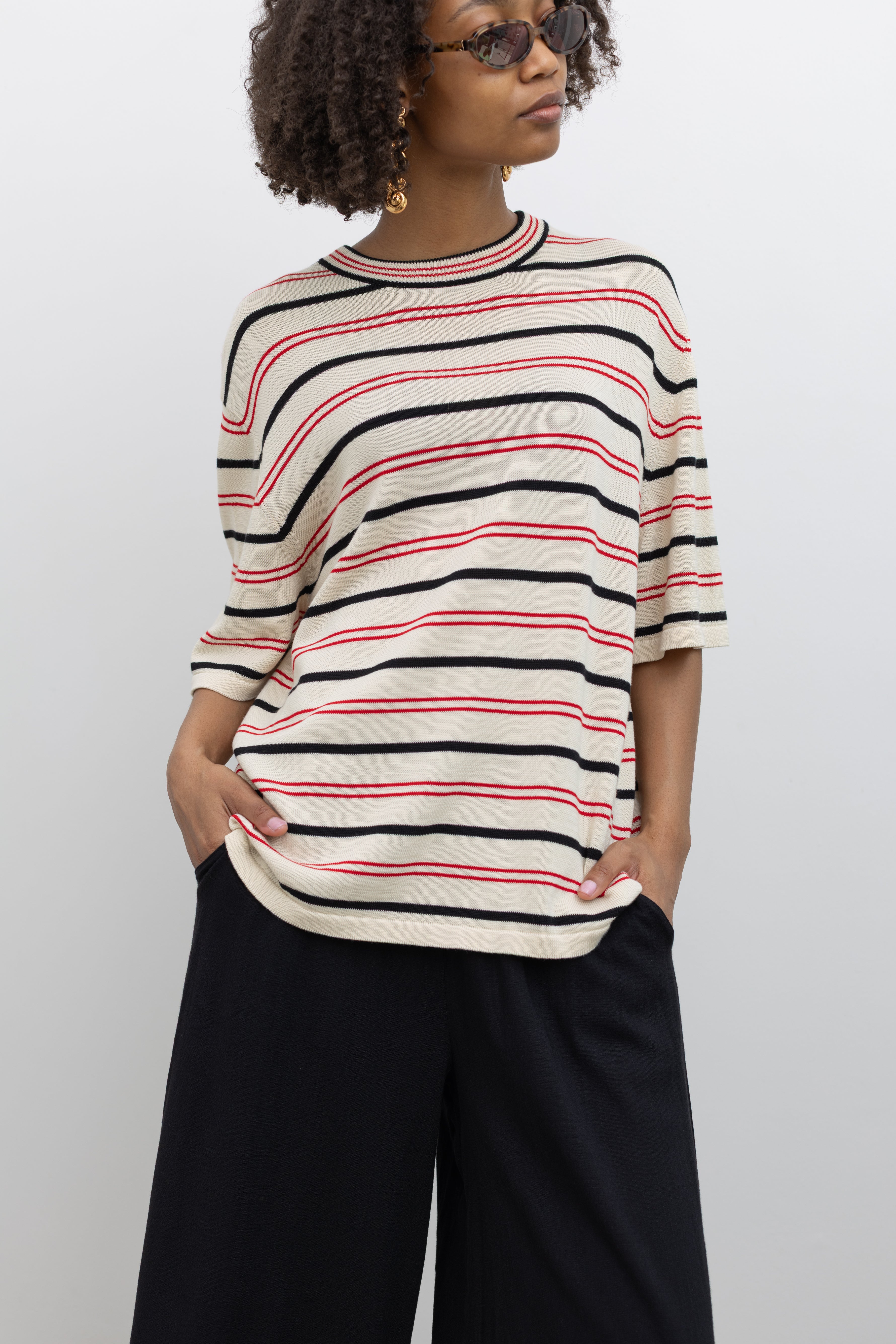 Model wearing elevated casual staple in a Coreda oversized t-shirt featuring a classic crew neck, red and black stripes in varying widths on an ecru background at Alas Eius.
