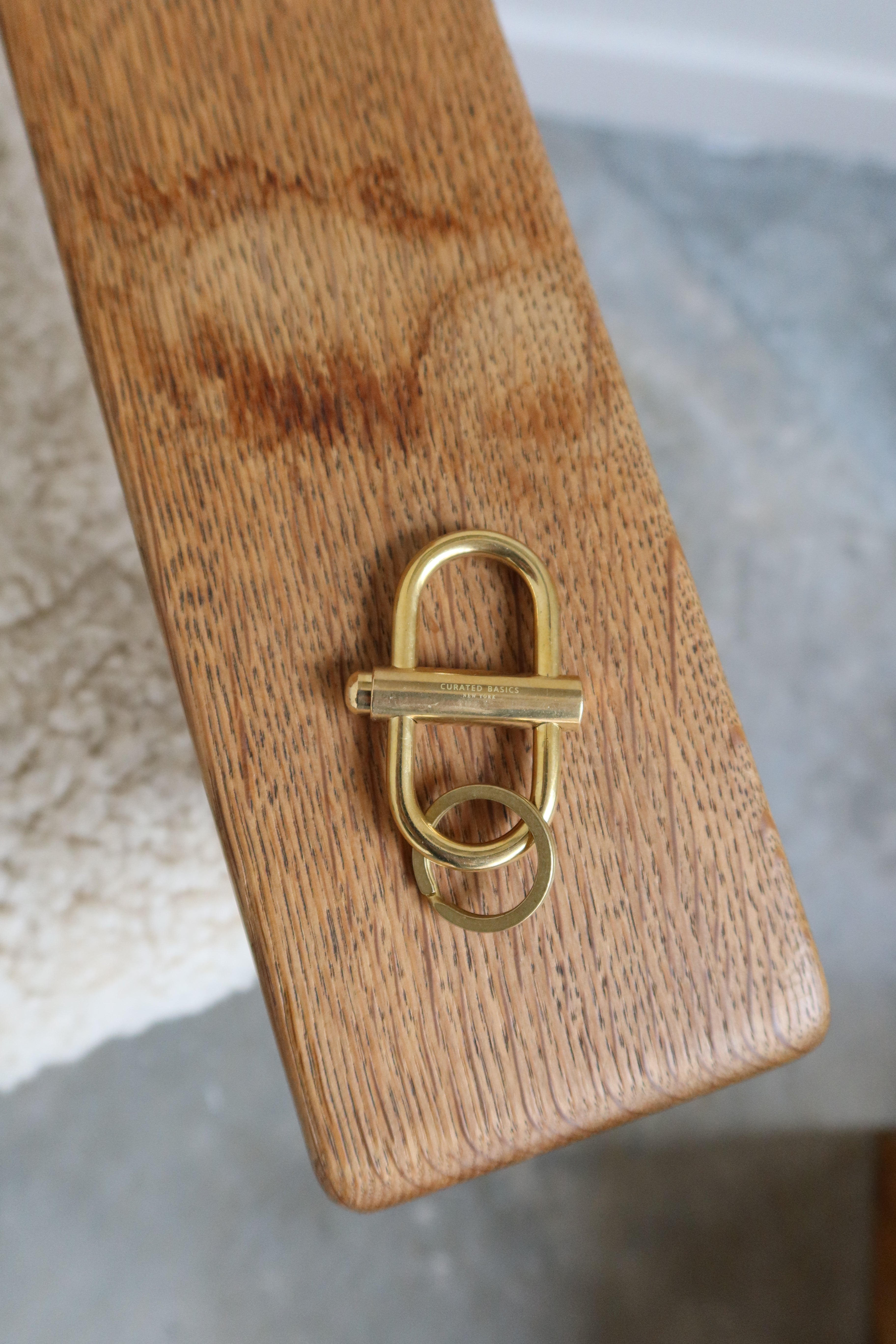 A Curated Basics brand oval brass lock keychain on a wood surface at Alas Eius. 