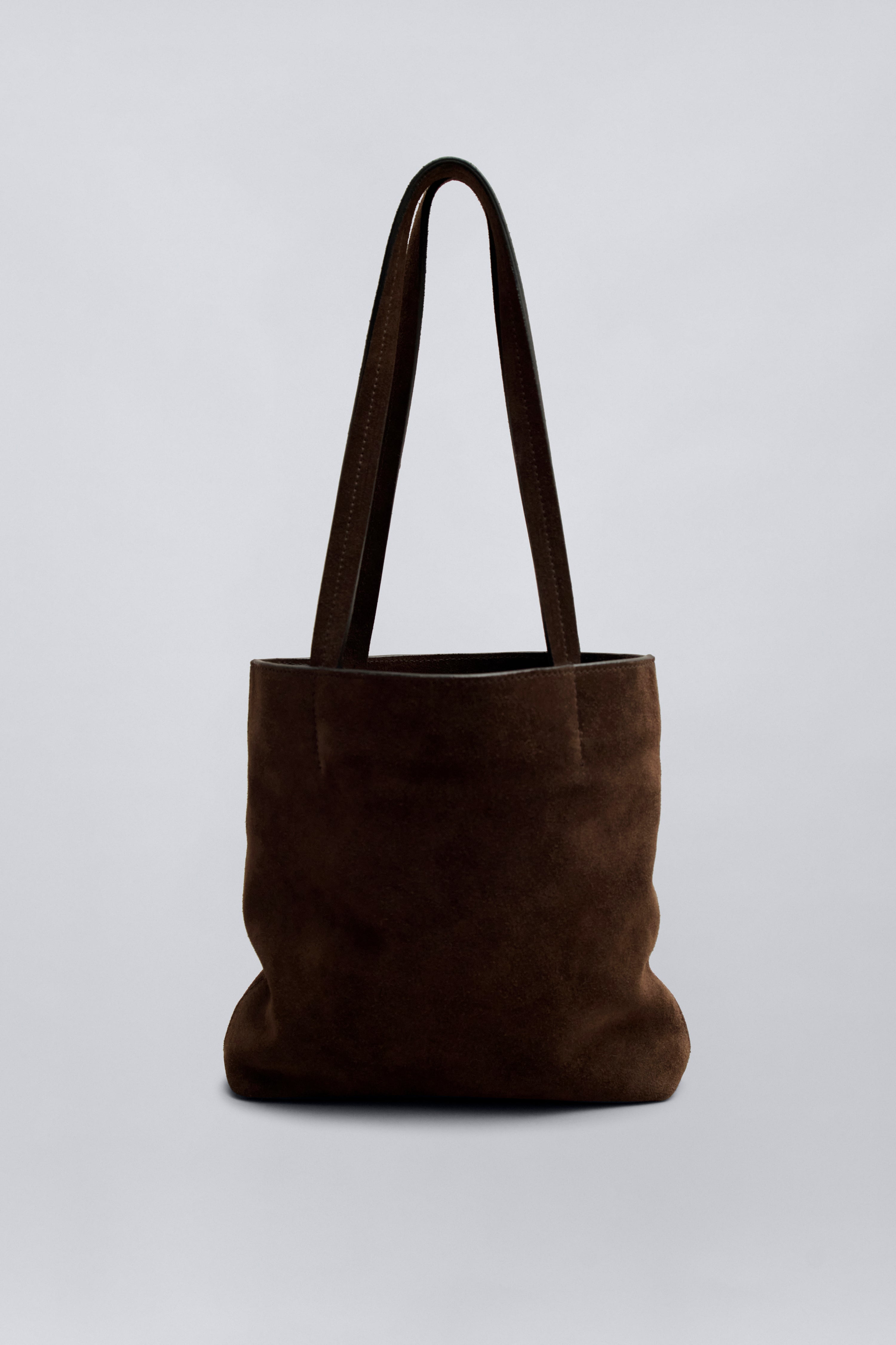 Front product view of a chic and elevated classic structured tote by Kallmeyer in rich brown suede, dual flat shoulder straps, and a permanent canvas drawstring pouch opening with leather toggles at Alas Eius. 