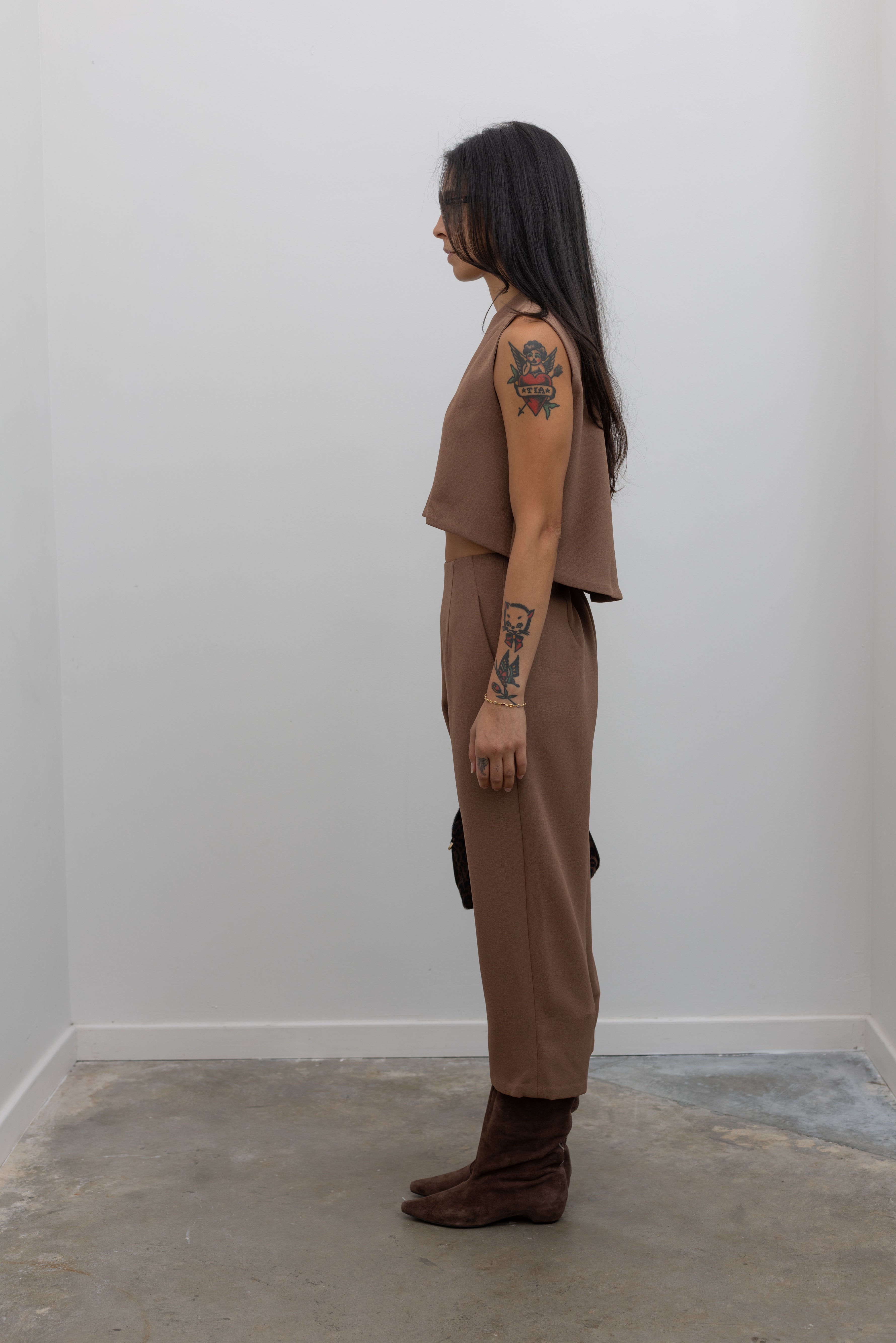 Full side view of a woman standing wearing spring fashion in the Kaarem Cacao Sua Tapered Trouser Pocket Pant with the coordinating top to make a set paired with brown suede boots at Alas Eius.