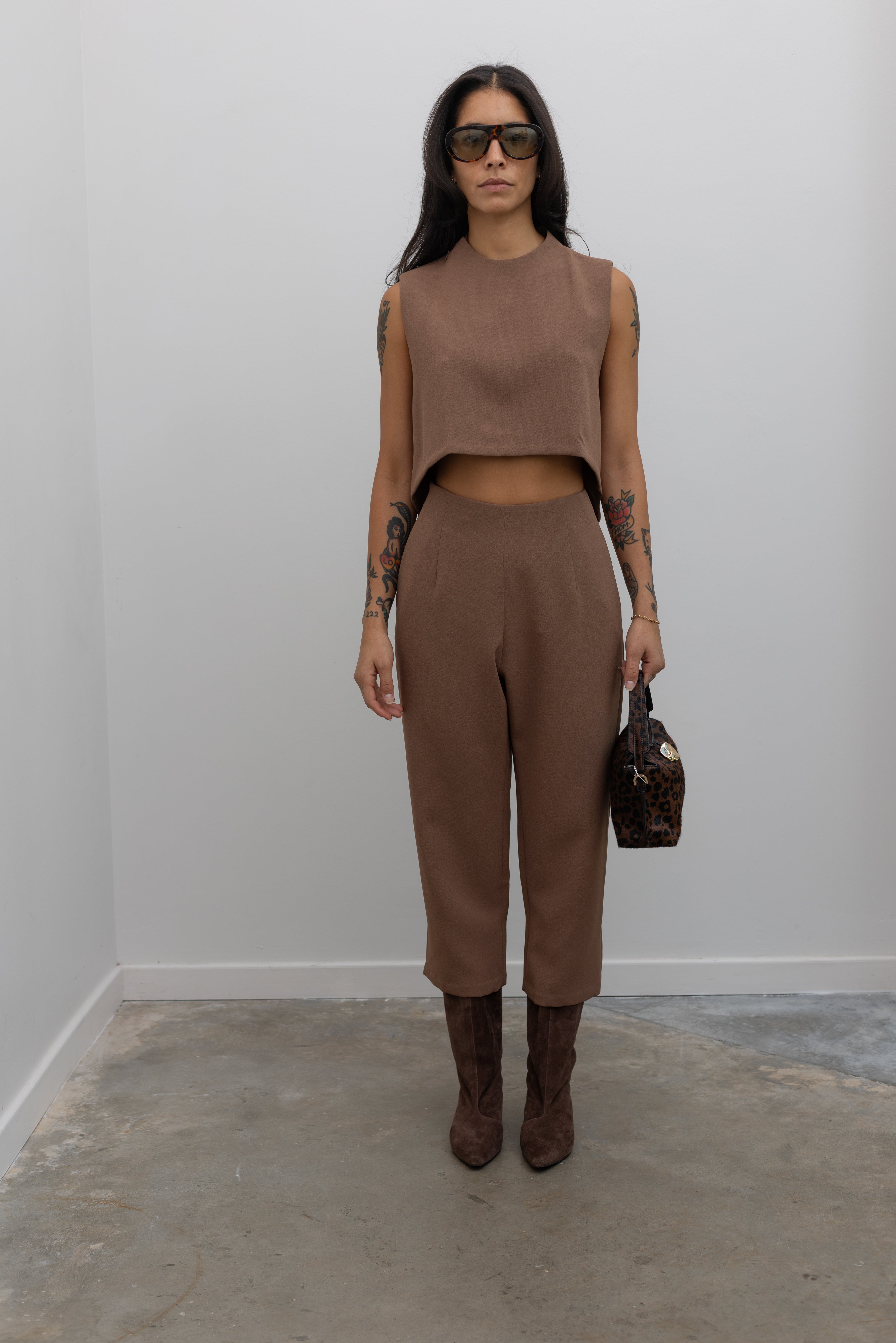 Full front view of a woman standing wearing spring fashion in the Kaarem Cacao Sua Tapered Trouser Pocket Pant with the coordinating top to make a set paired with brown suede boots at Alas Eius.