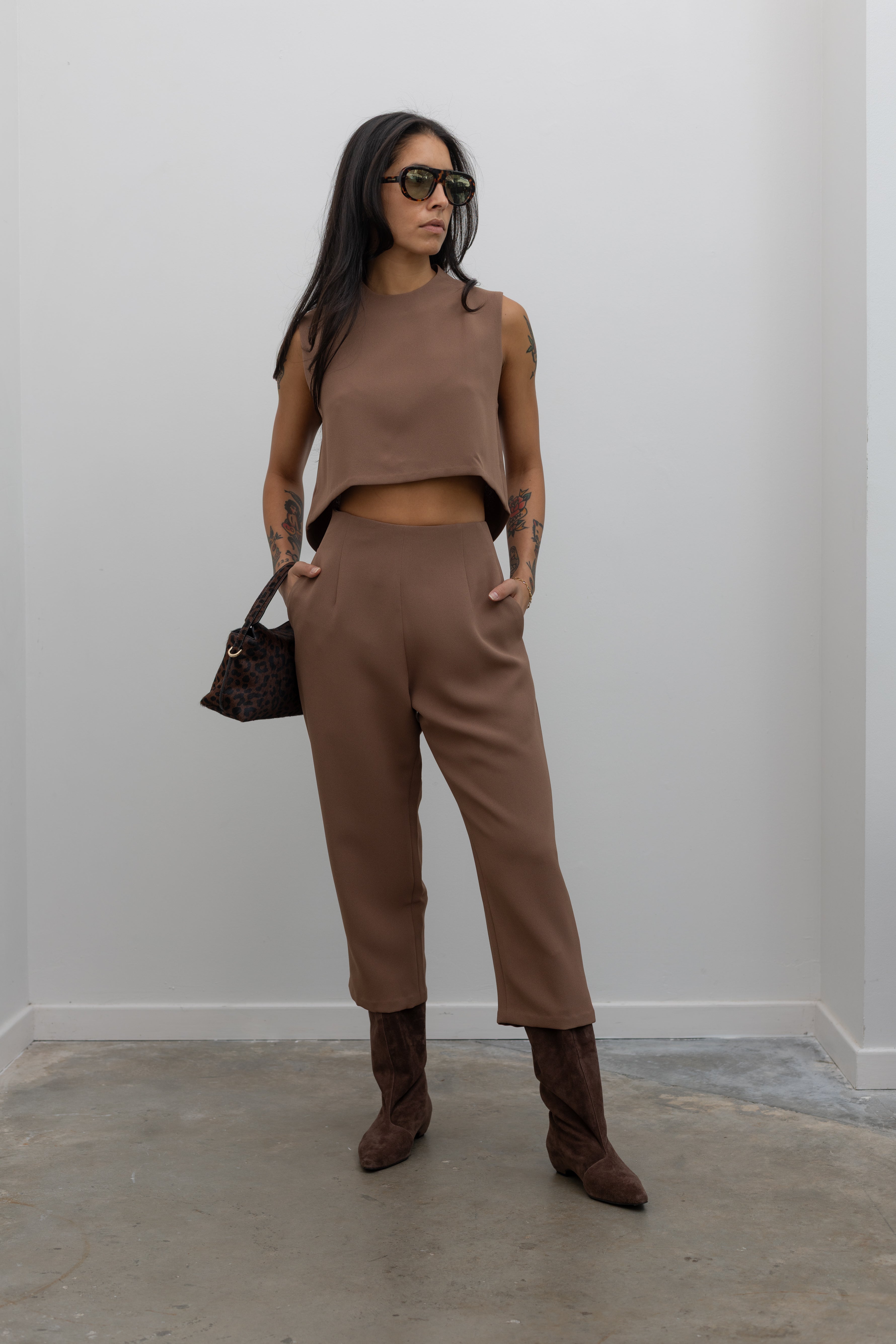 Full front view of a woman standing wearing spring fashion in the Kaarem Cacao Sua Tapered Trouser Pocket Pant with the coordinating top to make a set paired with brown suede boots at Alas Eius.