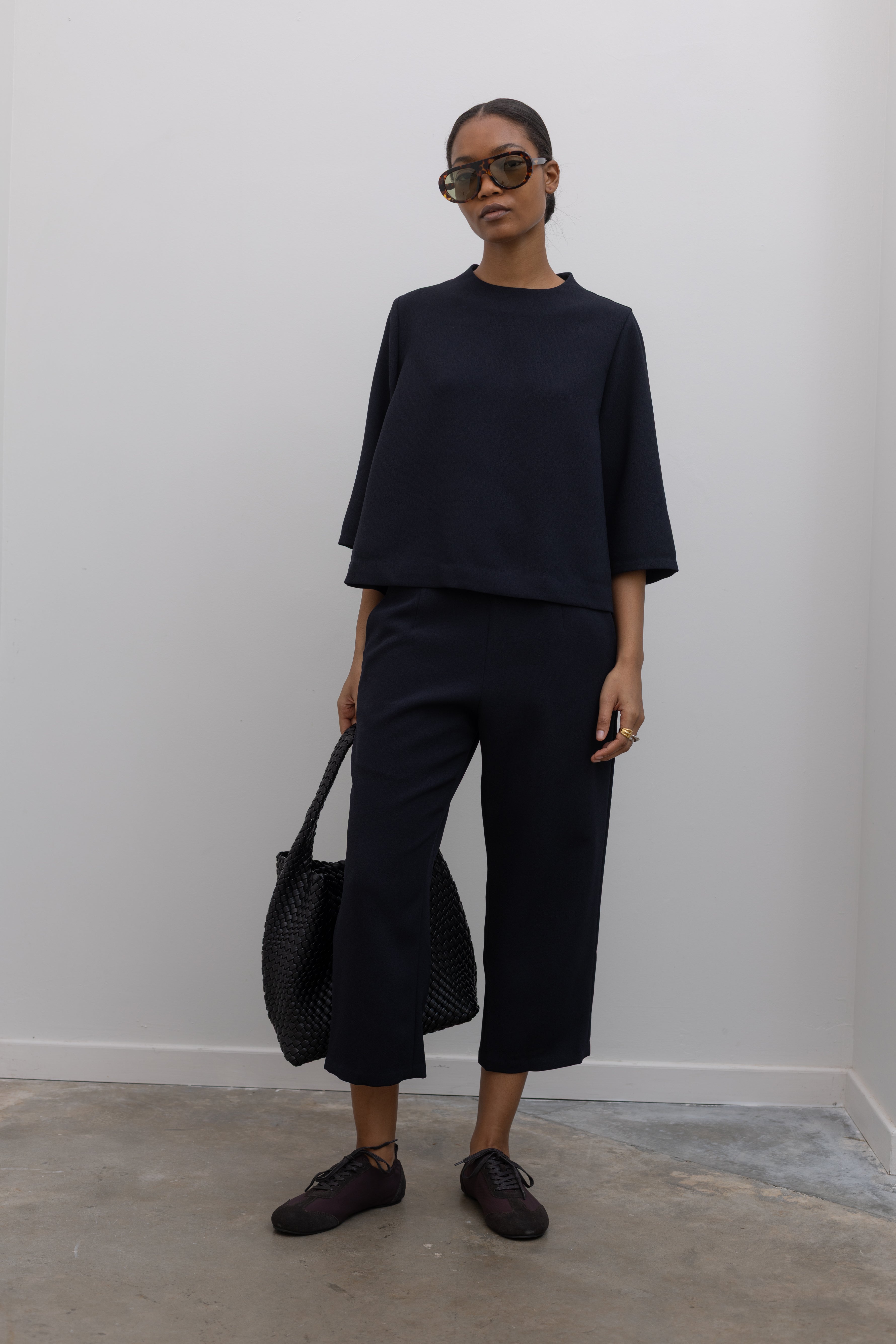 Full length front view of a woman standing wearing the Kaarem Deep Navy Sua Tapered Trouser Pocket Pant with the coordinating top to make the perfect capsule wardrobe set at Alas Eius