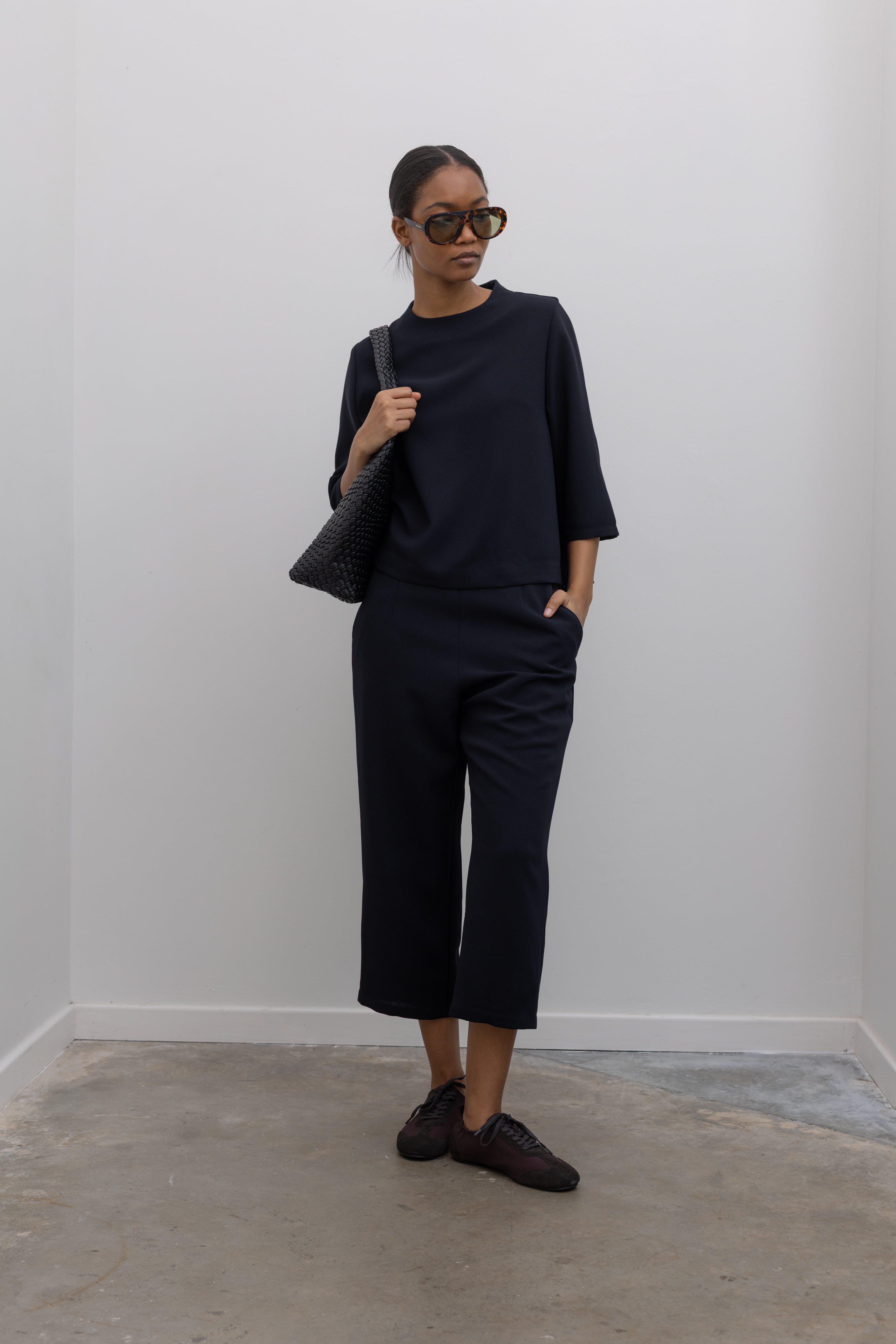 Full length front view of a woman standing wearing the Kaarem Deep Navy Sua Tapered Trouser Pocket Pant with the coordinating top to make the perfect capsule wardrobe set at Alas Eius