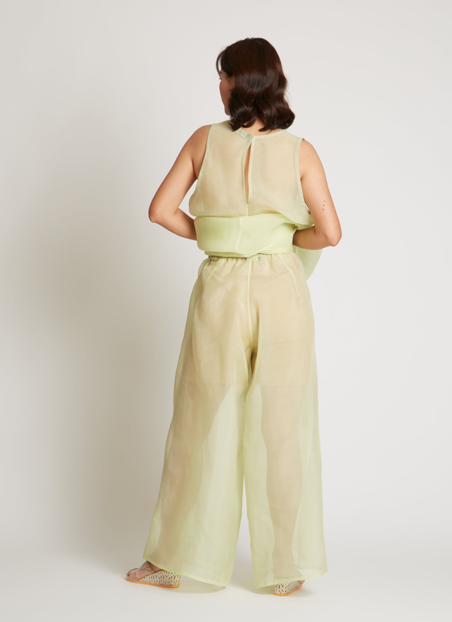 Back view of the Kaarem SS26 Sheer Green Rice Marble Pleated Silk Organza Pant featuring a wide-leg silhouette, deep side pleats, and finished by a single artisan with a hand-drawn pattern and a delicate blind-hem stitch, featuring an elastic waistband and side pockets for practical ease at Alas EIus.